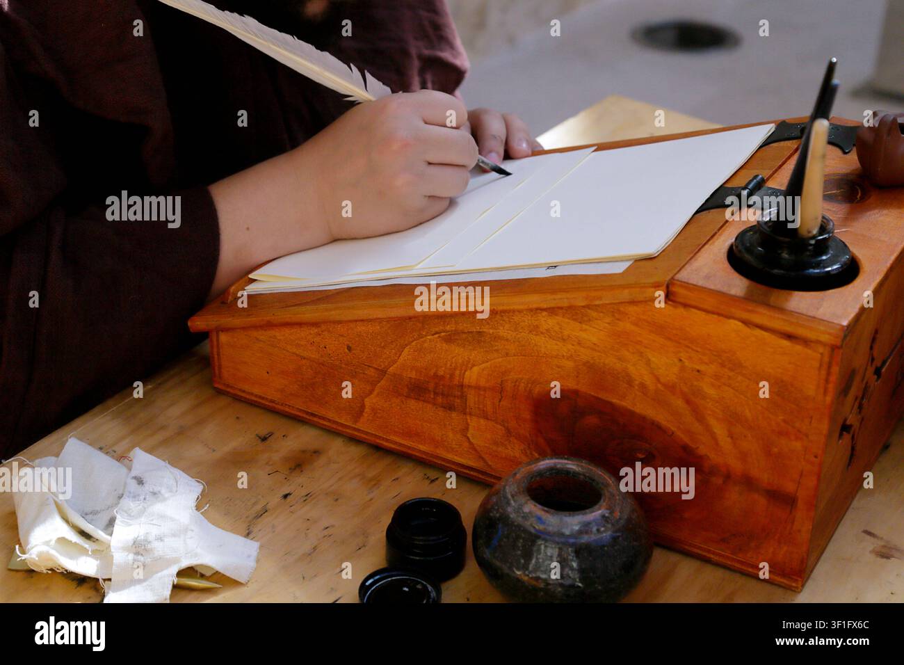 Person schreibt mit einer Feder auf Pergamentblättern an einem traditionellen hölzernen Schreibtisch. Stockfoto