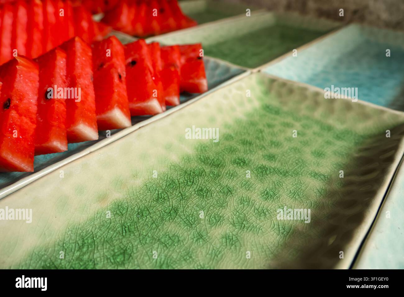 Eine geschnittene Wassermelone rote Frucht grüne Keramikplatte Sommer-Snack saftiges Fruchtfleisch Foodfotografie Samen dreieckige Scheibe Tischplatte Nahaufnahme Stockfoto