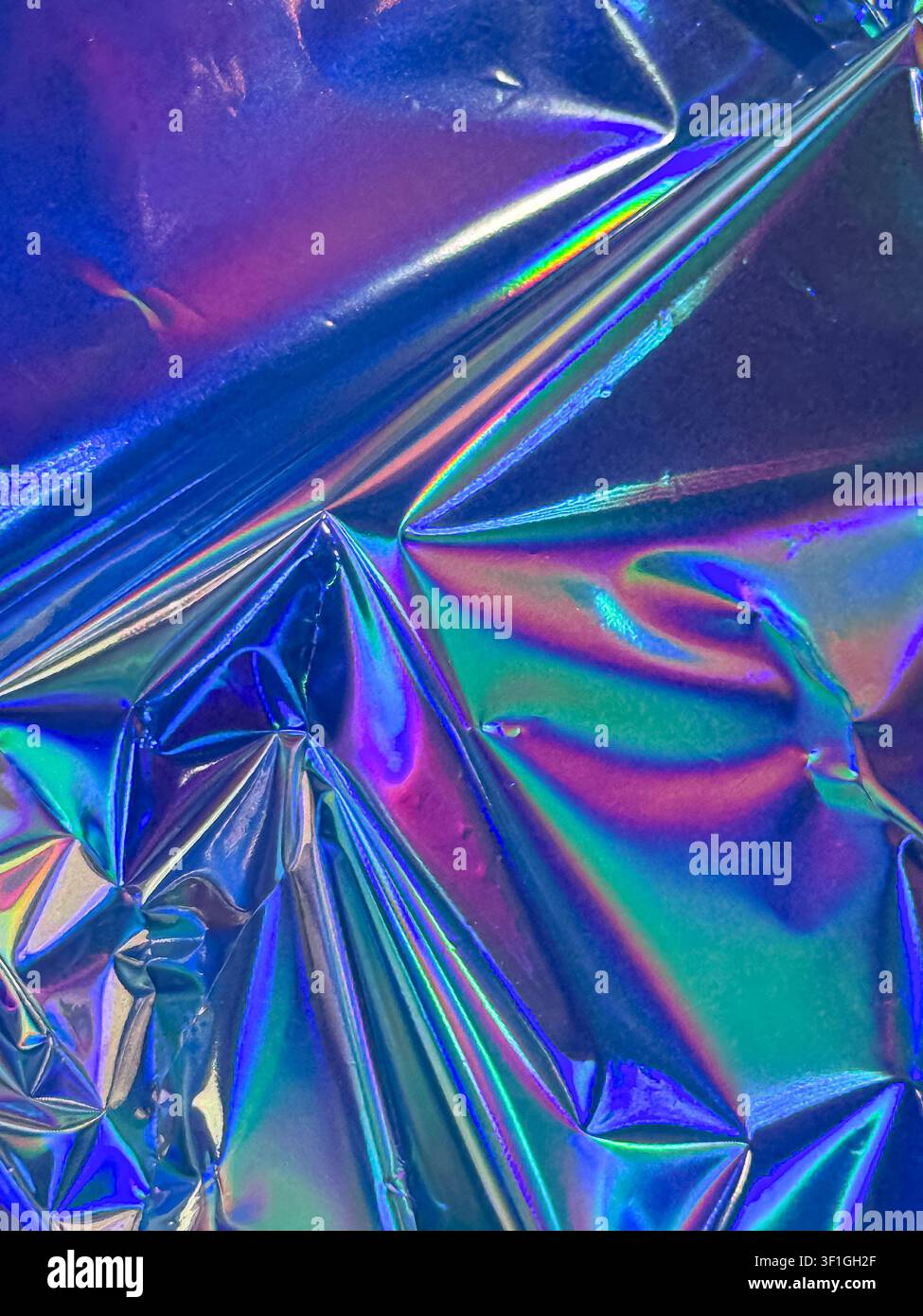 Abstrakter Hintergrund, der gefältiges irisierendes holografisches Material zeigt, das ein Farbspektrum einschließlich Blau, Lila und Grün reflektiert. Hervorhebung von mir Stockfoto