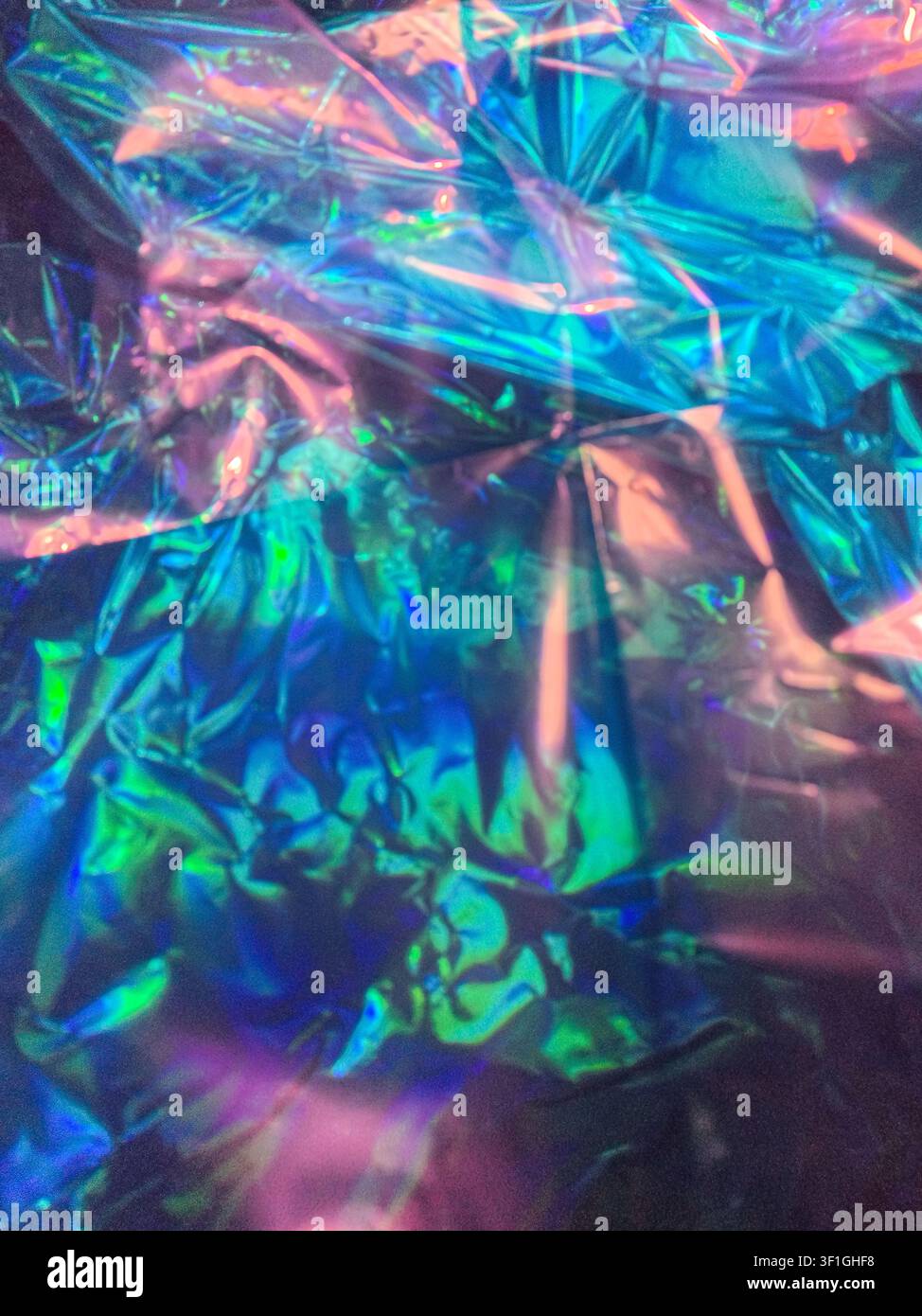 Reflektierendes strukturiertes Material zeigt lebendige blaue, grüne und rosa Lichtspektren. Nahaufnahme einer abstrakten Ansicht einer zerknitterten Oberfläche mit dynamischem Lichtreflex Stockfoto