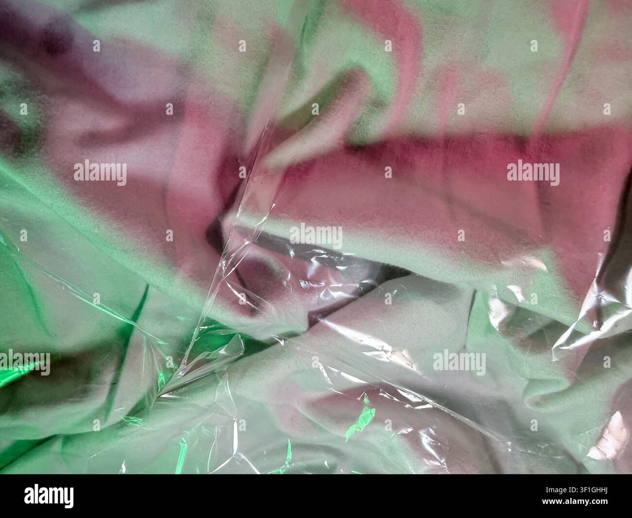 Nahaufnahme einer Stofftextur mit lebhaftem rosa und grünem Batikmuster. Weiche Stofffalten erzeugen Tiefe, wobei klarer Plastikfolie Glanz und Reflexion hinzufügt Stockfoto