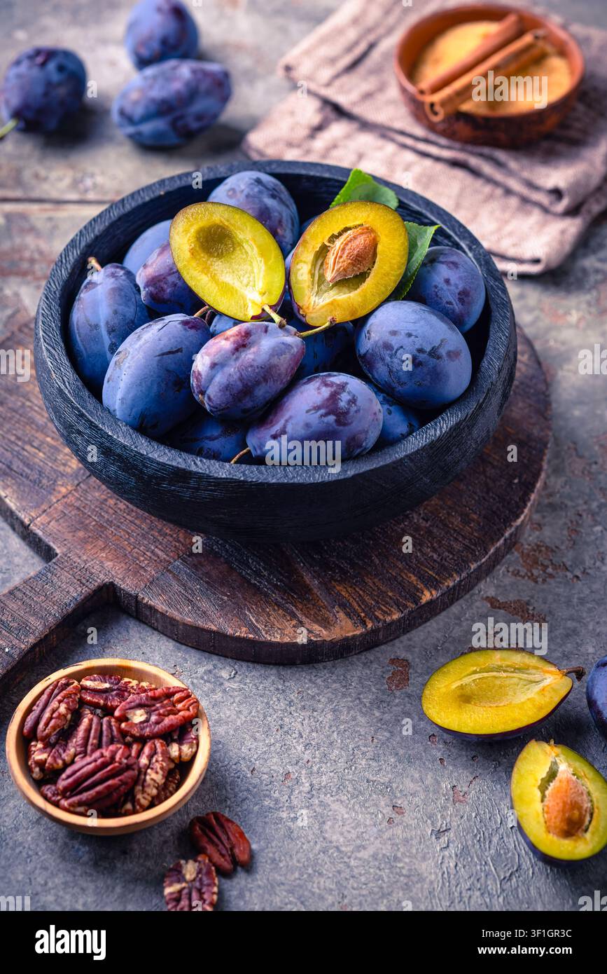 Frische reife Pflaumen in einer rustikalen Schüssel auf einem Holzbrett, ein gesunder Obstsnack Stockfoto