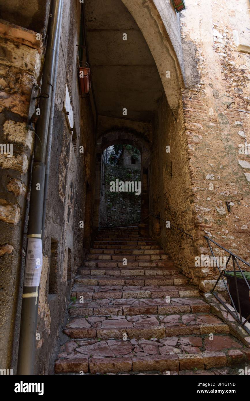 Vertikale Aufnahme einer mittelalterlichen Steintreppe, die durch einen historischen gewölbten Durchgang mit verwitterten Ziegelwänden in der Hügelstadt Stroncone aufsteigt, U Stockfoto