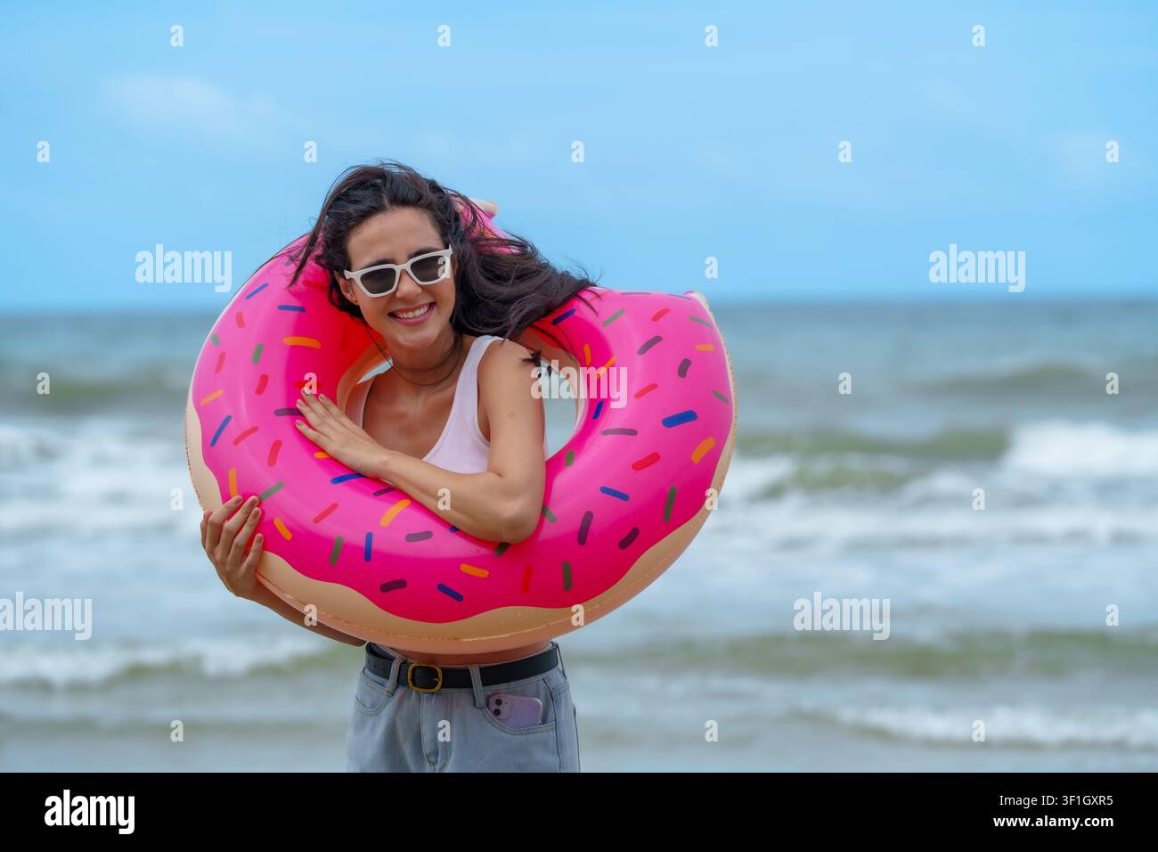 Fröhlicher Moment am Strand fängt Freunde ein, die den Sommer am Meer mit einem bunten, donutförmigen Schwimmring genießen. Lebendige Atmosphäre und verspielter Geist schaffen bleibende Eindrücke Stockfoto
