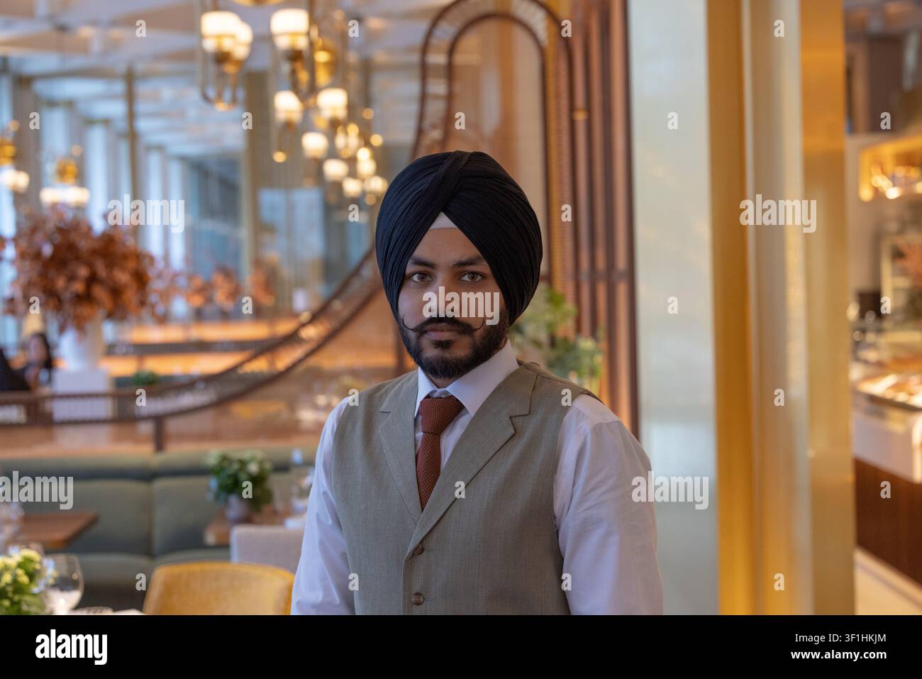 Porträt eines professionellen indischen Sikh-Hospitality-Mitarbeiters, der einen traditionellen Turban trägt und in einem luxuriösen Hotel-Fin-Dining-Restaurant steht Stockfoto