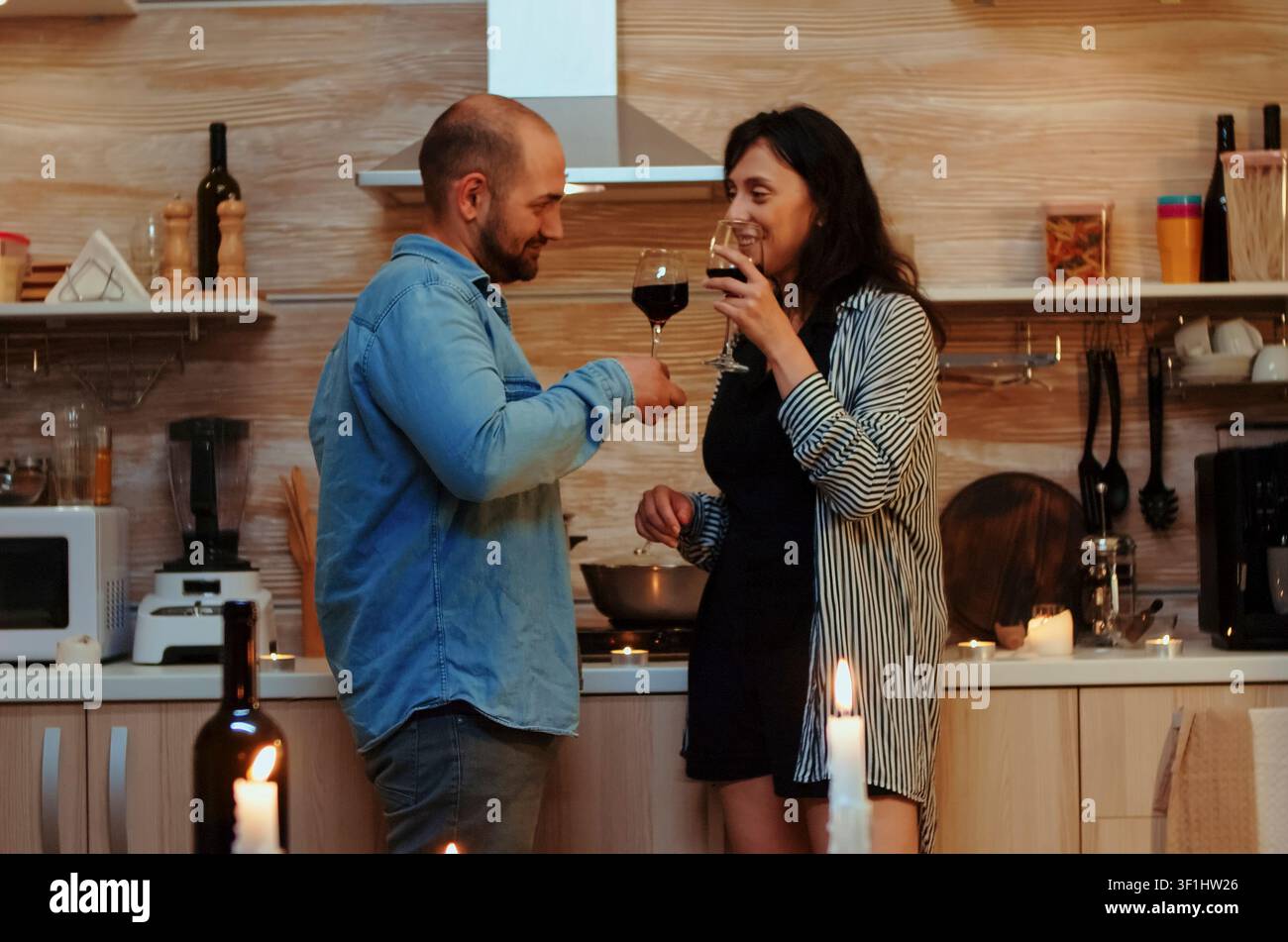 Junges Paar teilt ein romantisches Küchen-Date mit Rotwein, Gespräch und einer gesunden Mahlzeit während eines intimen Abendessens zu Hause. Stockfoto