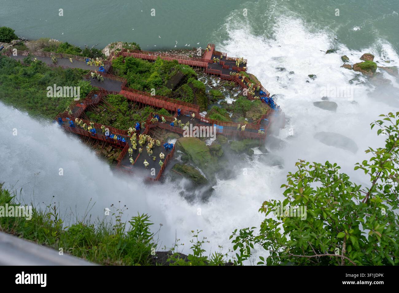 Eine Hochwinkel-Horizontalaufnahme, die auf Menschenmassen von Touristen hinunterblickt, die gelbe und blaue Regenponchos tragen, auf hölzernen Beobachtungsplattformen und Gehwegen am t Stockfoto