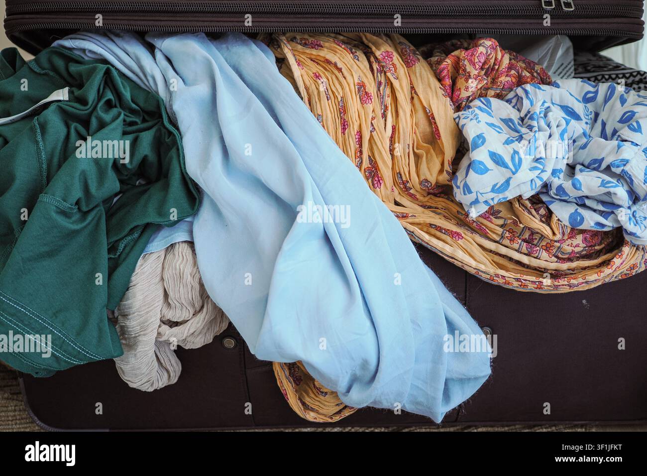 Kleidung stapelt sich in einem offenen Koffer auf dem Boden Stockfoto