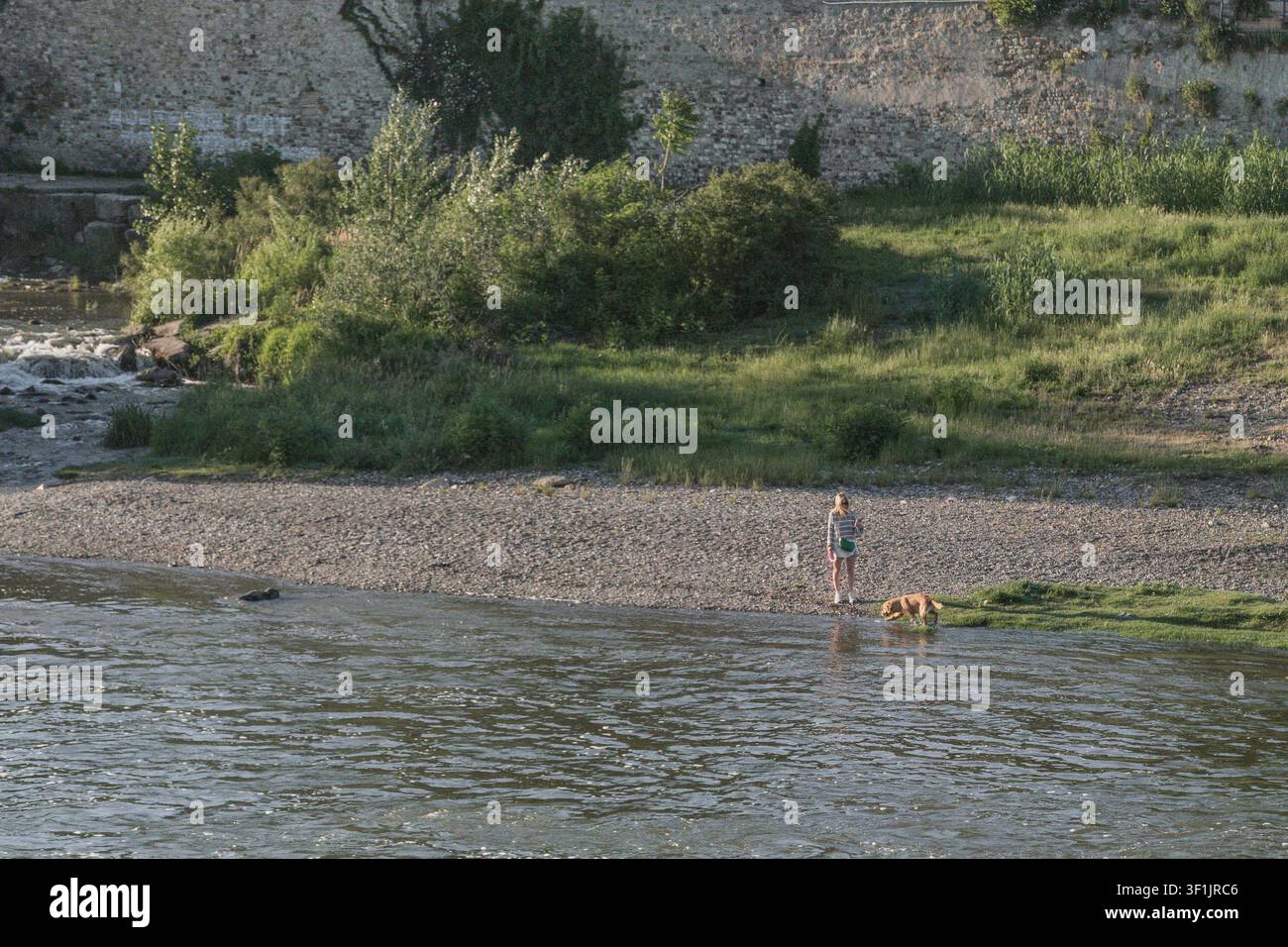 Frau mit Hund und Haus im Hintergrund am Ufer des Arno nahe Florenz, Italien Stockfoto