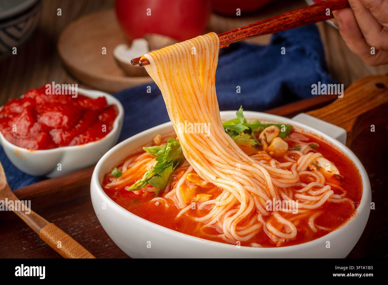 Traditionelle chinesische Tomatensuppen-Nudeln in einer weißen Schüssel mit Holzgriff, garniert mit Pilzen und Grünzeug, serviert auf einem dunklen Holztray. Stockfoto