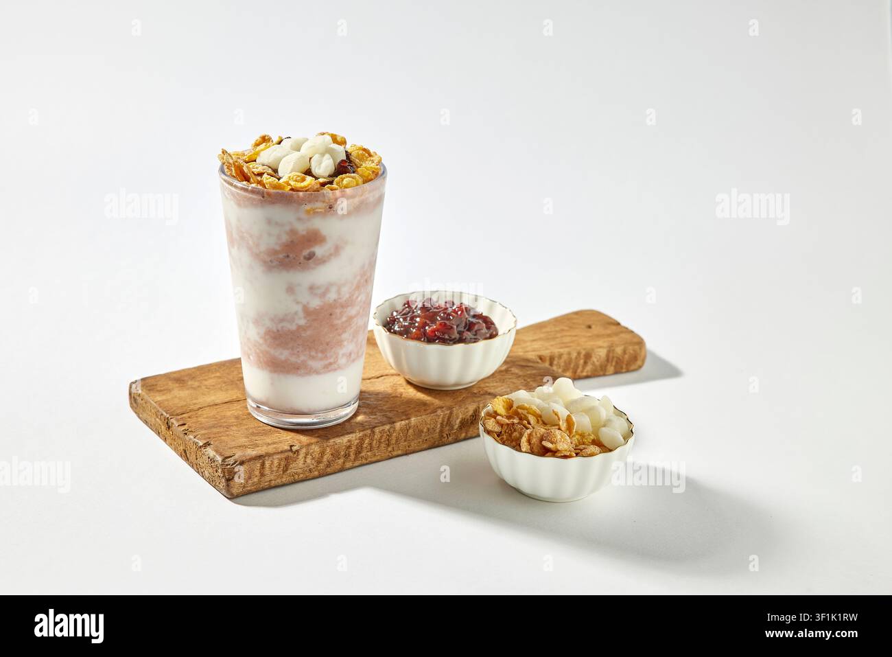 Granola-Yoghurt-Parfait-Getränk in einem hohen Glas, serviert auf einem Holztablett mit Schüsseln mit Belägen wie roten Bohnen, Cornflakes und Nüssen auf einem hellgrauen Hintergrund Stockfoto