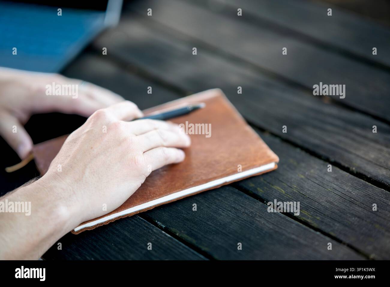 Hände, die auf einem braunen Notizbuch mit Stift auf dunklem Holztisch ruhen, Konzept für einen Arbeitsplatz im Freien. Stockfoto