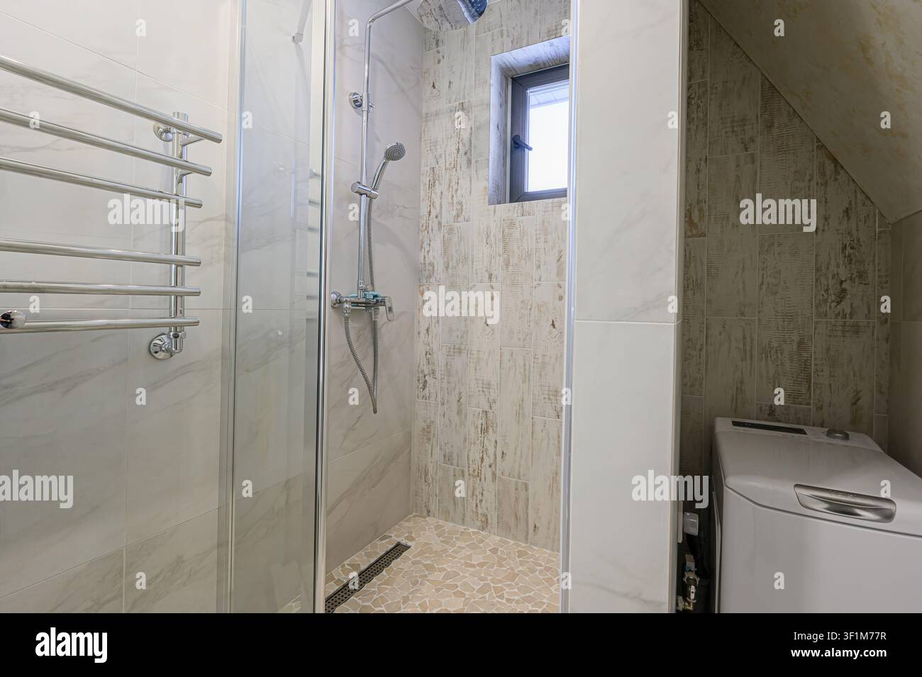 Modernes Badezimmer mit einer Glasduschkabine, einem Handtuchwärmer, einem kleinen Fenster und einer Waschmaschine in platzsparendem Design Stockfoto