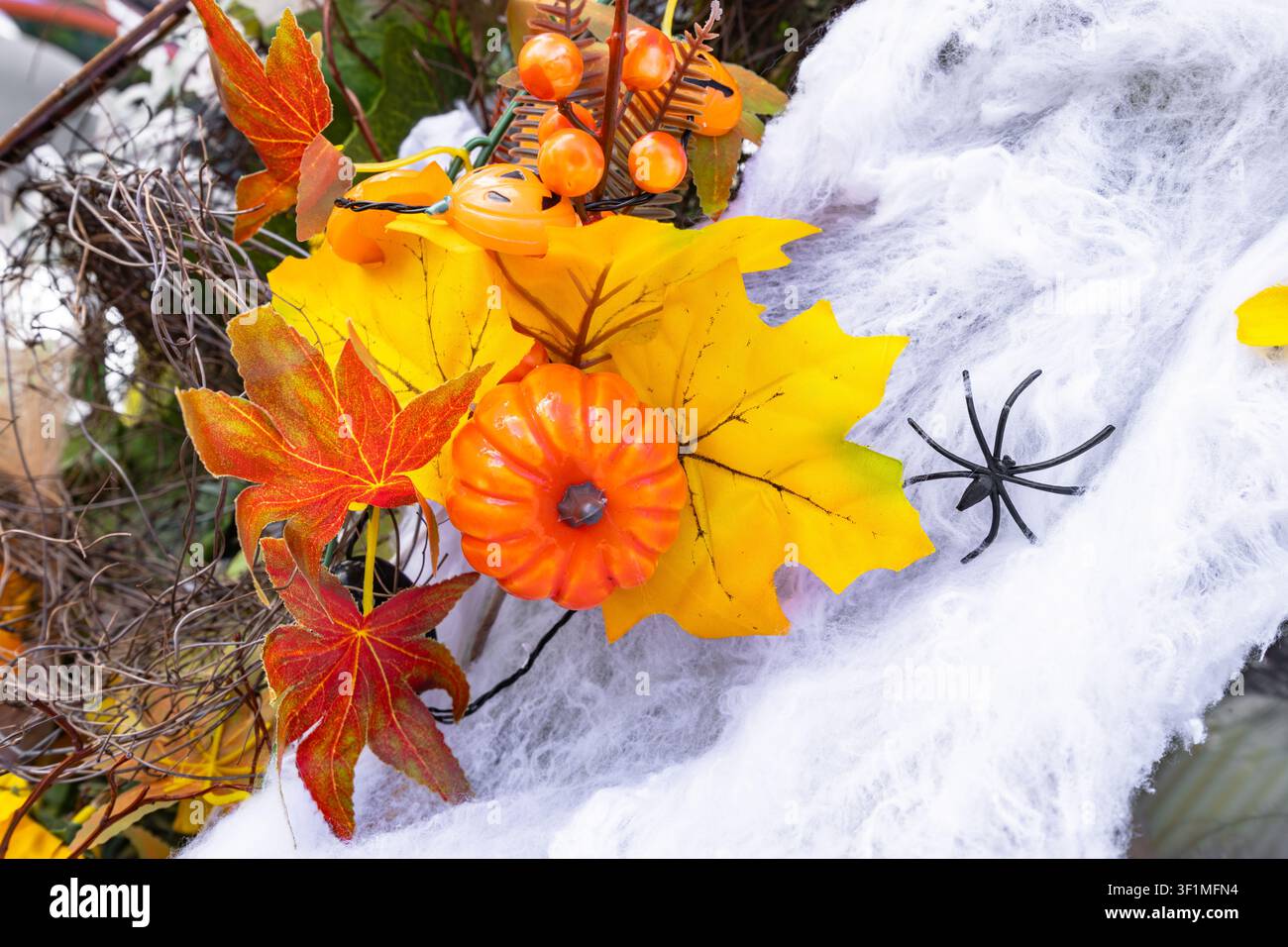 Halloween-Dekoration-Kranz mit künstlichen orangefarbenen Kürbissen, Herbstblättern und einer schwarzen Spinne auf weißem Netz Stockfoto