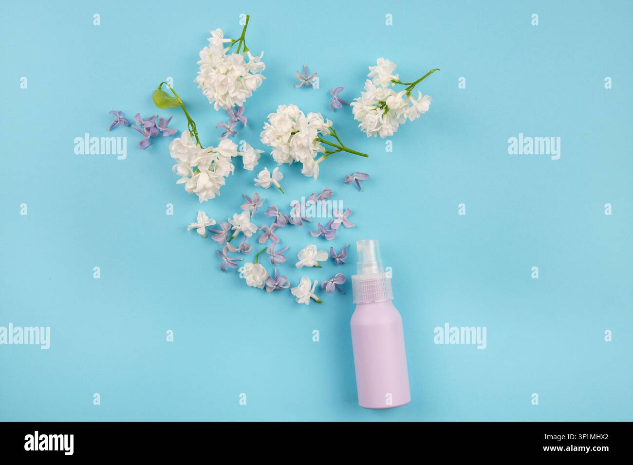 Hausgemachtes Hydrosol oder Hydrolat, auch bekannt als Blütenwasser oder Fliederhydrosol. Lila Sprühflasche auf blauem Hintergrund, mit Flieder verziert. Stockfoto
