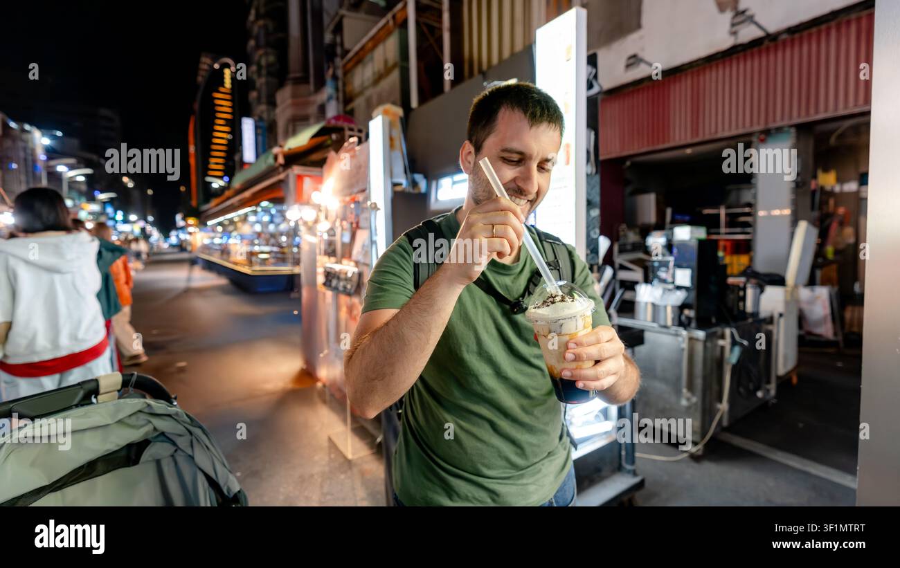 Ein Reisender genießt Oreo-Bubble-Tea auf dem Liuhe-Nachtmarkt in Kaohsiung, Taiwan. Die lebhafte Nachtmarktatmosphäre bietet einzigartige Straßenessenerlebnisse Stockfoto