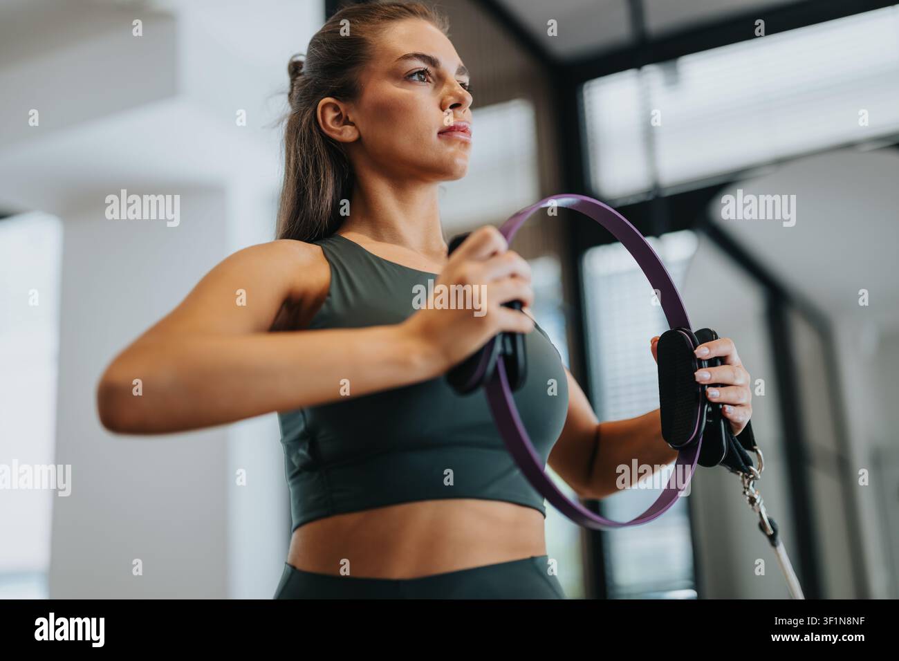 Junge Frau macht Pilates mit einem Widerstandsrings in einem hellen Fitnessstudio Stockfoto