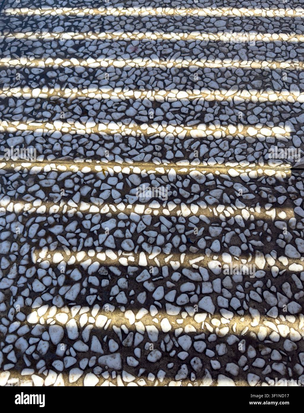 Abstrakter Hintergrund aus langen linearen Schatten, die über einen weißen Kiessteinpatio geworfen werden. - Smartphone-aufgenommenes Stockfoto