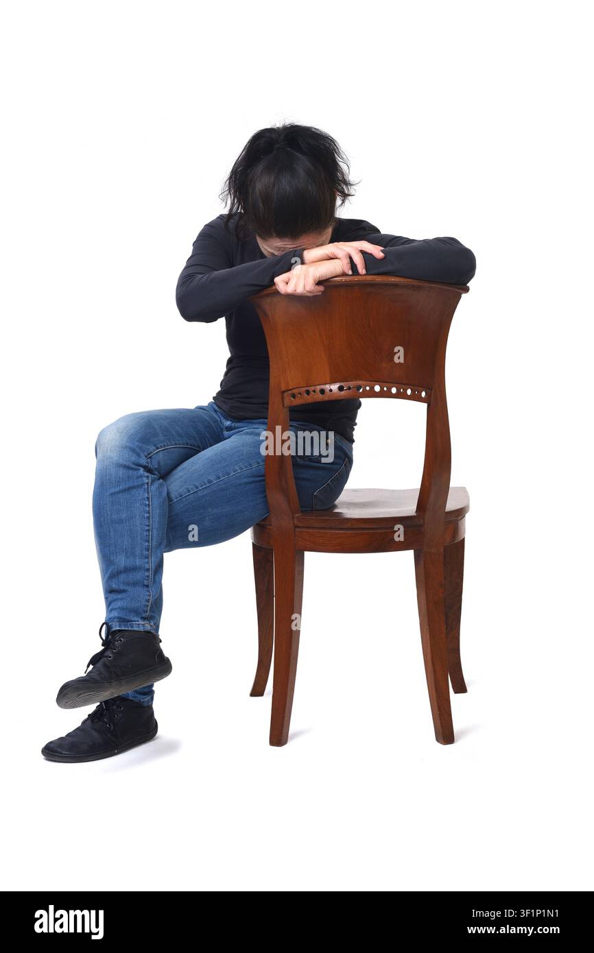 Vorderansicht einer Frau, die auf einem Stuhl sitzt, nach unten schaut und ihren Kopf mit den Händen bedeckt, wobei der Stuhl gegen einen weißen Hintergrund gedreht ist. Stockfoto