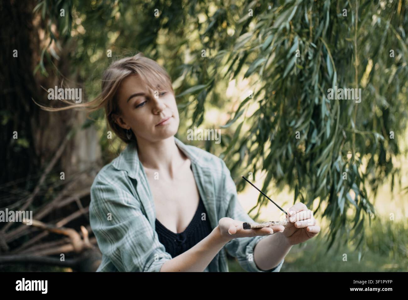 Frau hält brennenden Räucherstab im Freien. Spirituelle Reinigung, beruhigende Atmosphäre, Meditationshilfe, Outdoor-Ritual Stockfoto