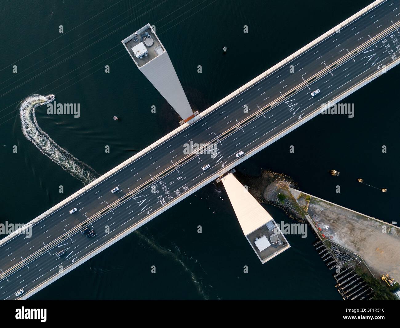 Luftaufnahme der Bolte-Brücke mit Verkehr, der über die mehrspurige Autobahn fließt, und einem kleinen Boot, das unterhalb in den Docklands, Victor, eine Spur im Wasser hinterlässt Stockfoto