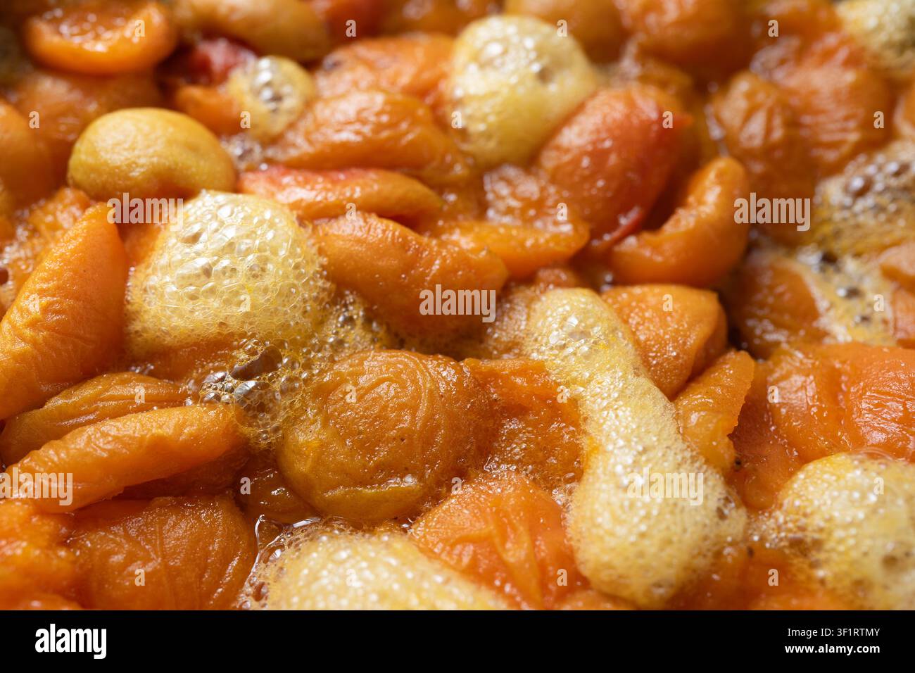 Nahaufnahme von frischen Aprikosen, die beim Kochen von hausgemachter Marmelade köcheln. Natürliche Fruchtkonserve mit Blasen während des Kochvorgangs. Stockfoto
