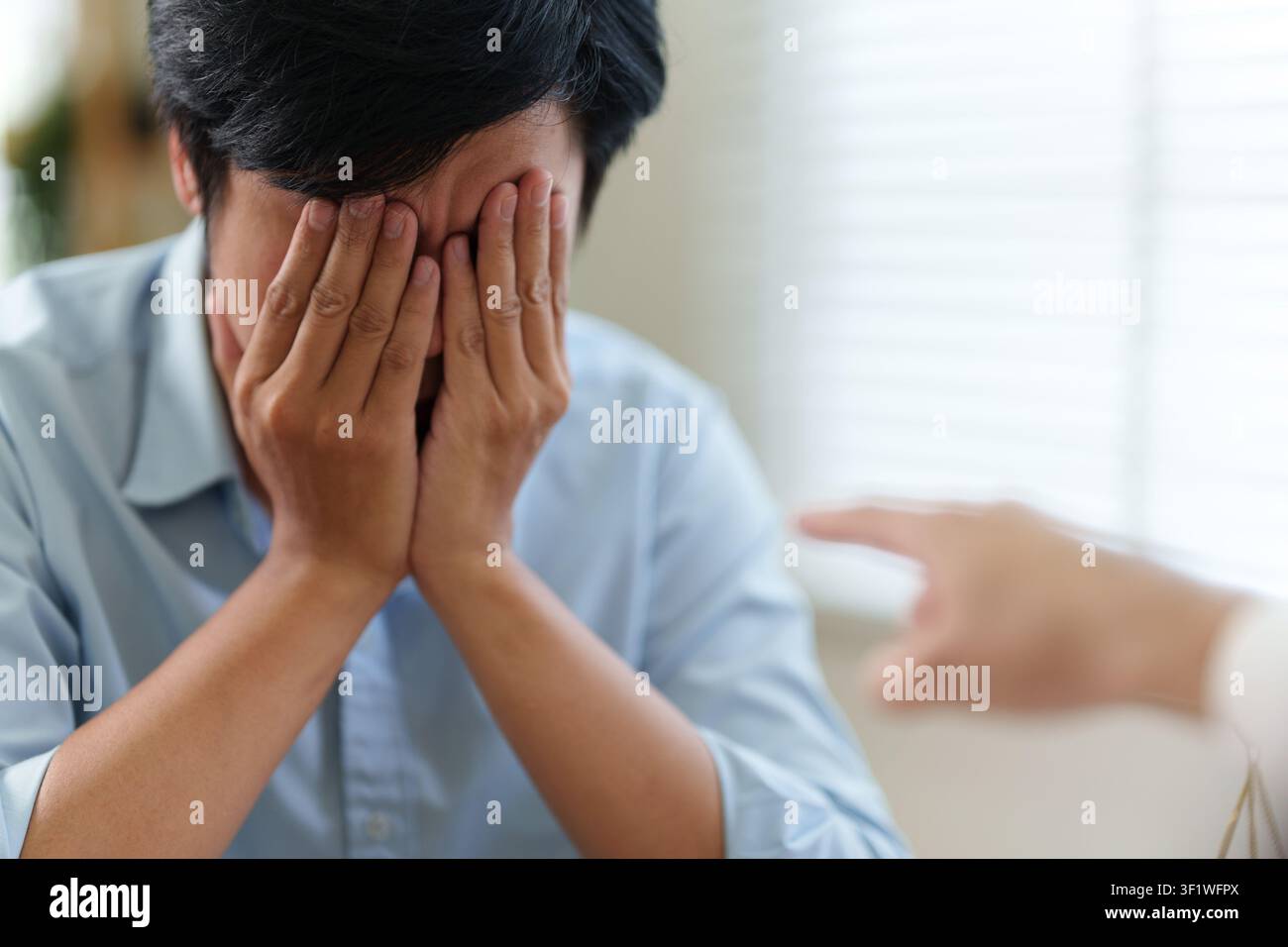 Gestresster asiatischer Geschäftsmann, der sein Gesicht während einer Anschuldigung und eines Konflikts am Arbeitsplatz bedeckt Stockfoto