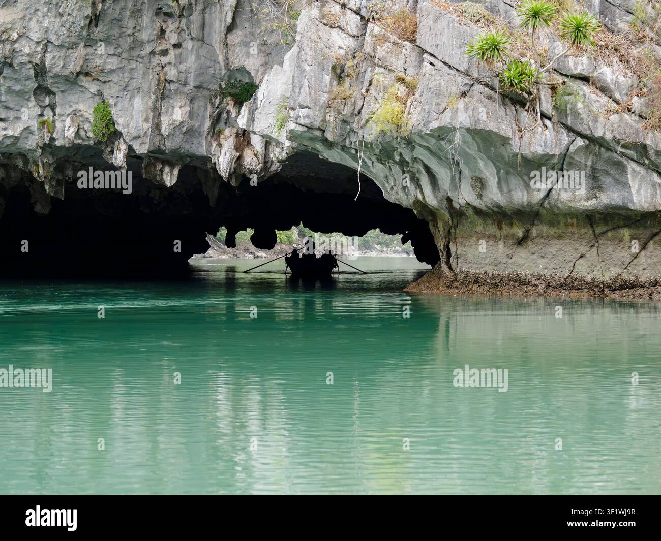 Kleines Ruderboot als Silhouette in einer Kalksteinhöhle auf ruhigem smaragdgrünem Wasser in der Lan Ha-Bucht, Vietnam. Stockfoto