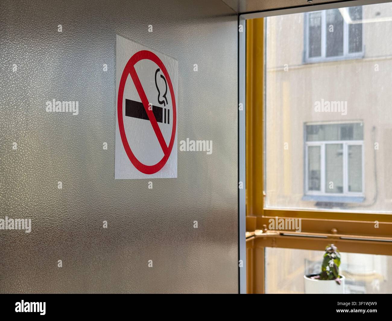 Rauchverbotsschild an einer Wand in einem Gebäude, Tageslicht strömt durch ein nahegelegenes Fenster. Mobilfoto Stockfoto