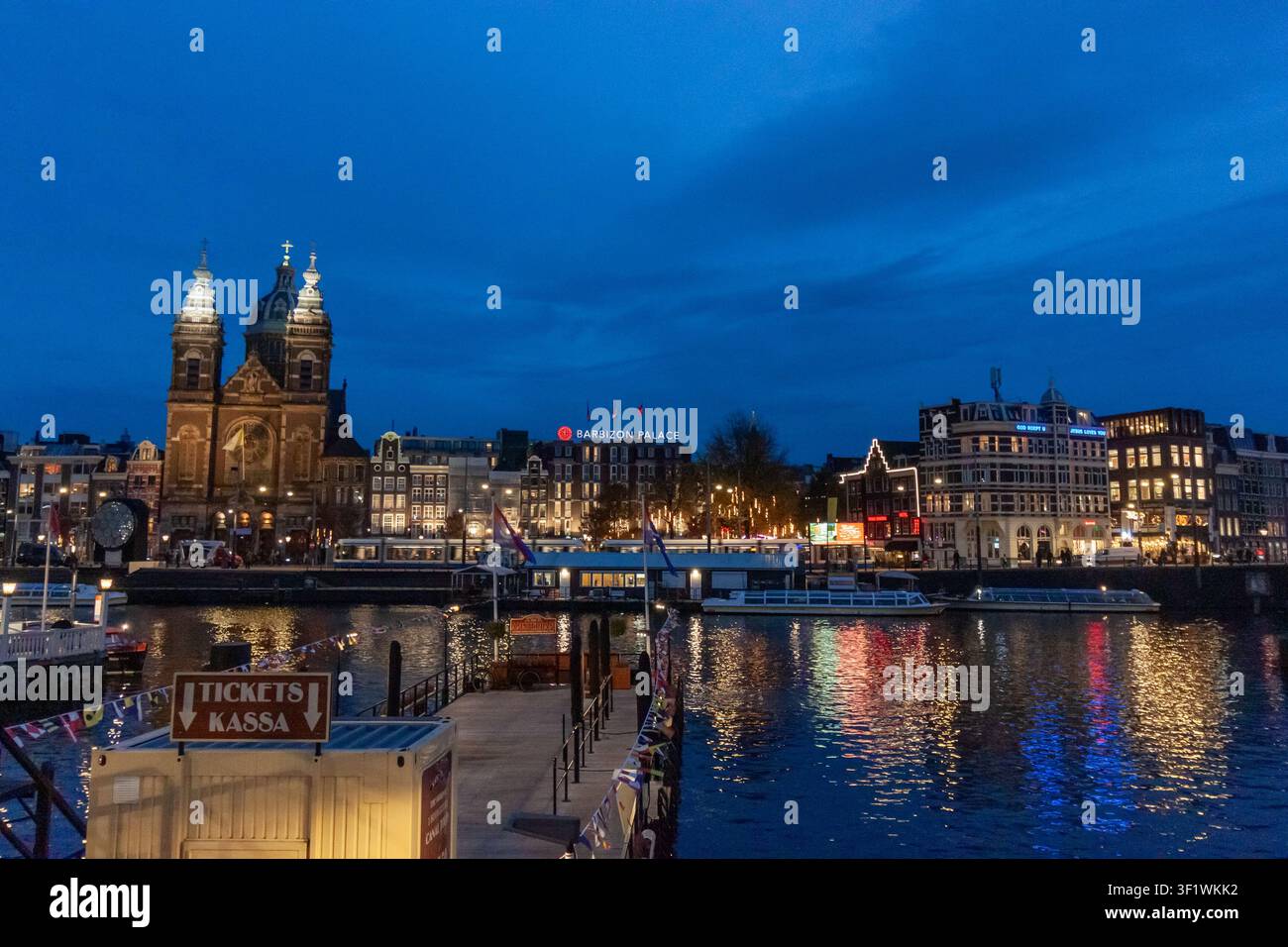 AMSTERDAM, NIEDERLANDE - 10. NOVEMBER 2025: Basilika des Heiligen Nikolaus und Stadtsilhouette bei Dämmerung über dem Kanal in Amsterdam, Niederlande Stockfoto