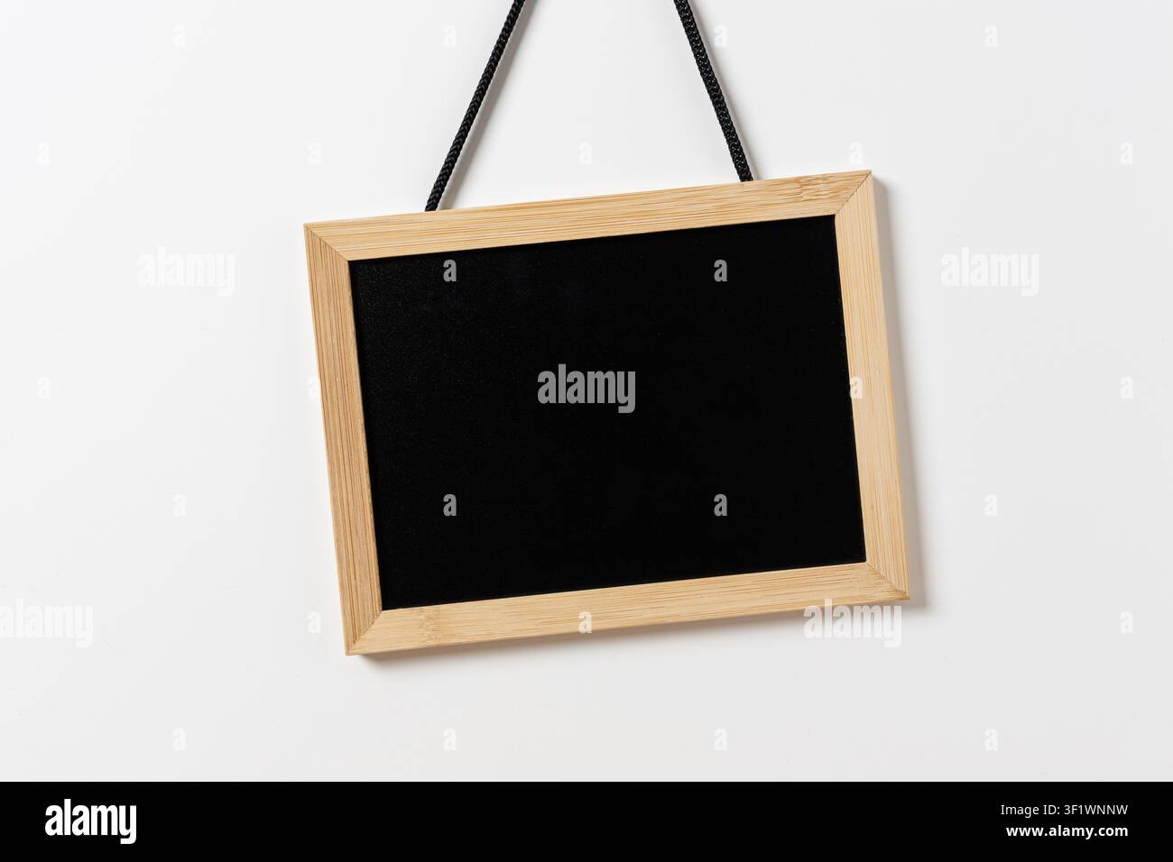 Leere Tafel mit Holzrahmen, die an einer weißen Wand hängt. Vorlagen-Mockup Stockfoto
