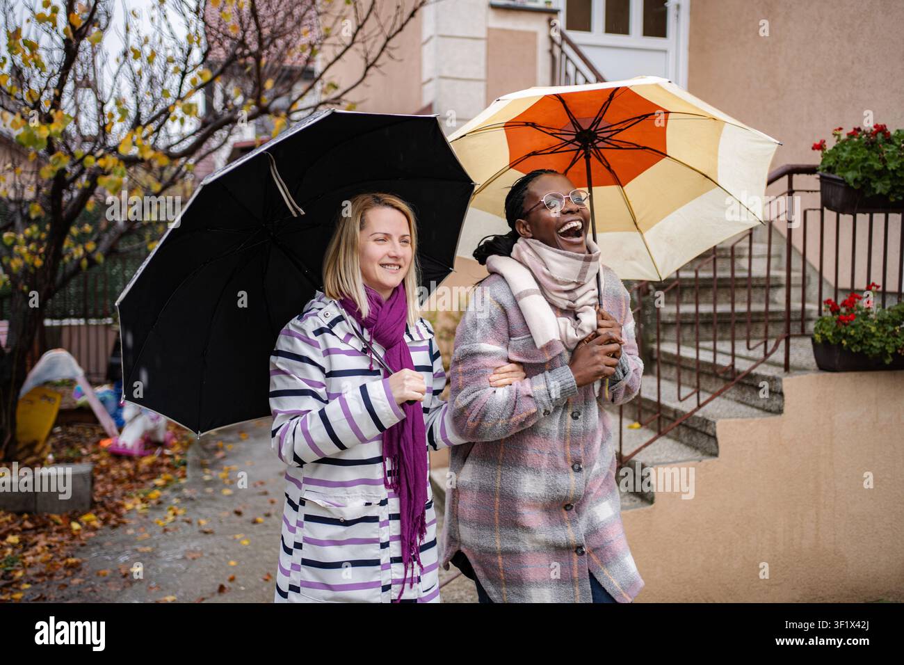 Verschiedene Freunde gehen und lachen, teilen Schirme im Herbstregen Stockfoto