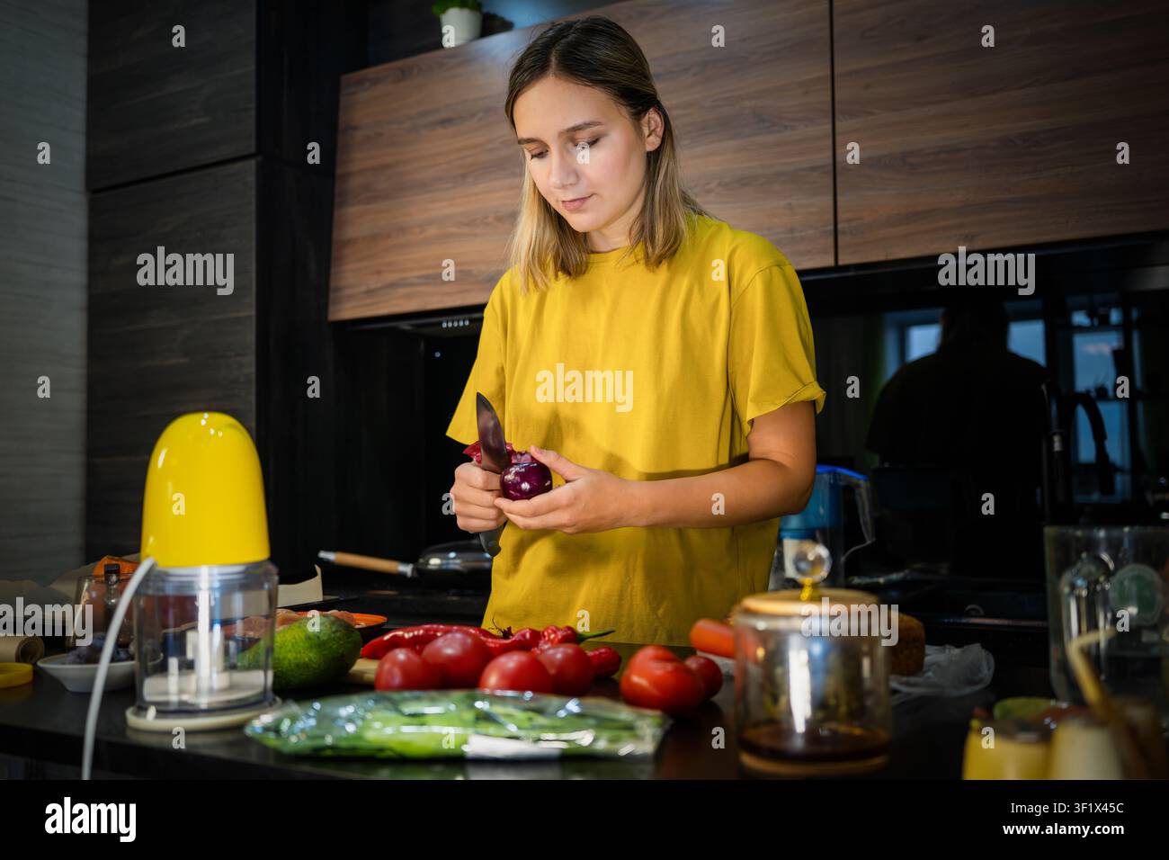 Junge Frau hackt frisches Gemüse auf einer Küchentheke, während sie eine gesunde hausgemachte Mahlzeit zubereitet. Hauskochen, ausgewogene Ernährung, frische Zutaten und Stockfoto