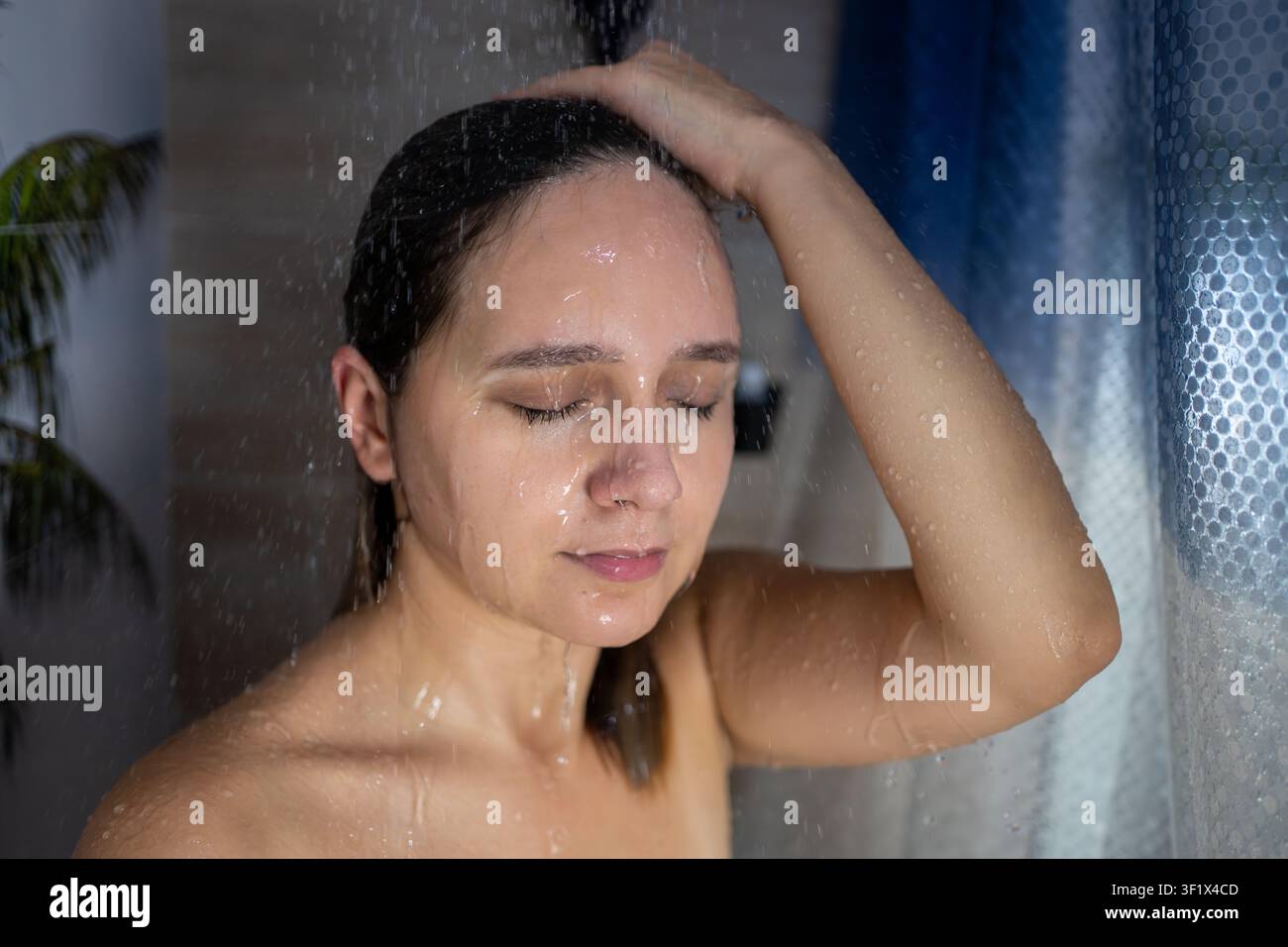 Junge Frau genießt eine erfrischende Dusche mit geschlossenen Augen, wäscht sich die Haare unter fließendem Wasser. Tägliche Hygiene, Selbstpflege, Wellness, Hautpflege und Entspannung Stockfoto
