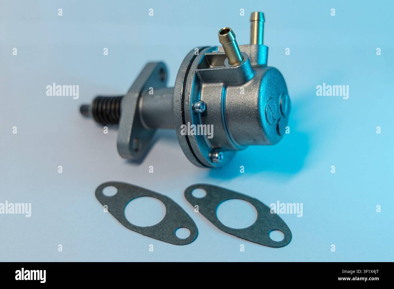 mechanische Kraftstoffpumpe mit Metallbeschlägen und einem federbelasteten Hebel, fotografiert mit passenden Gummidichtungen unter weißem und blauem Licht auf einem Stockfoto