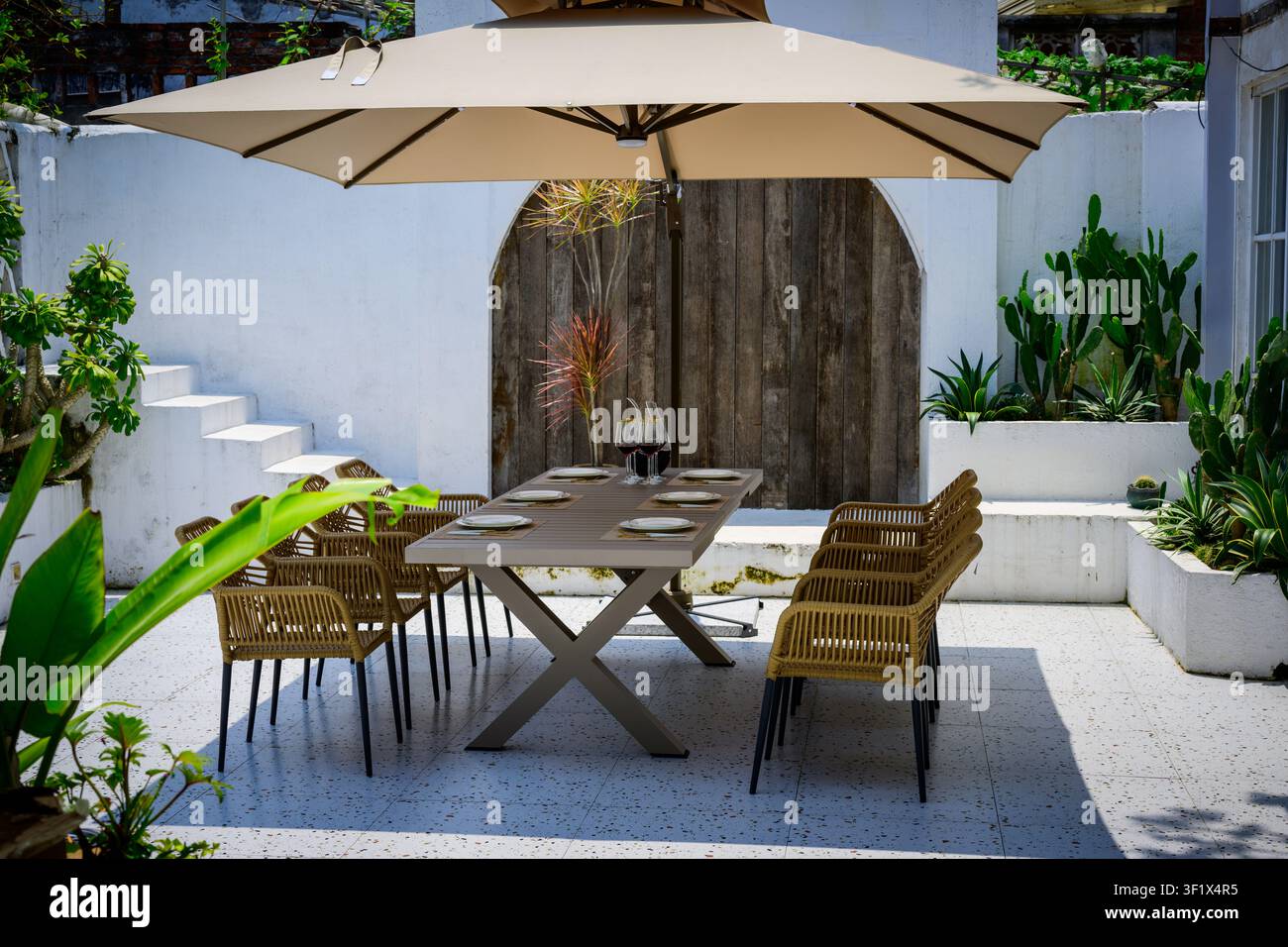 Ein Außenessbereich mit einem für acht Personen gedecktem Tisch unter einem Sonnenschirm. Stockfoto