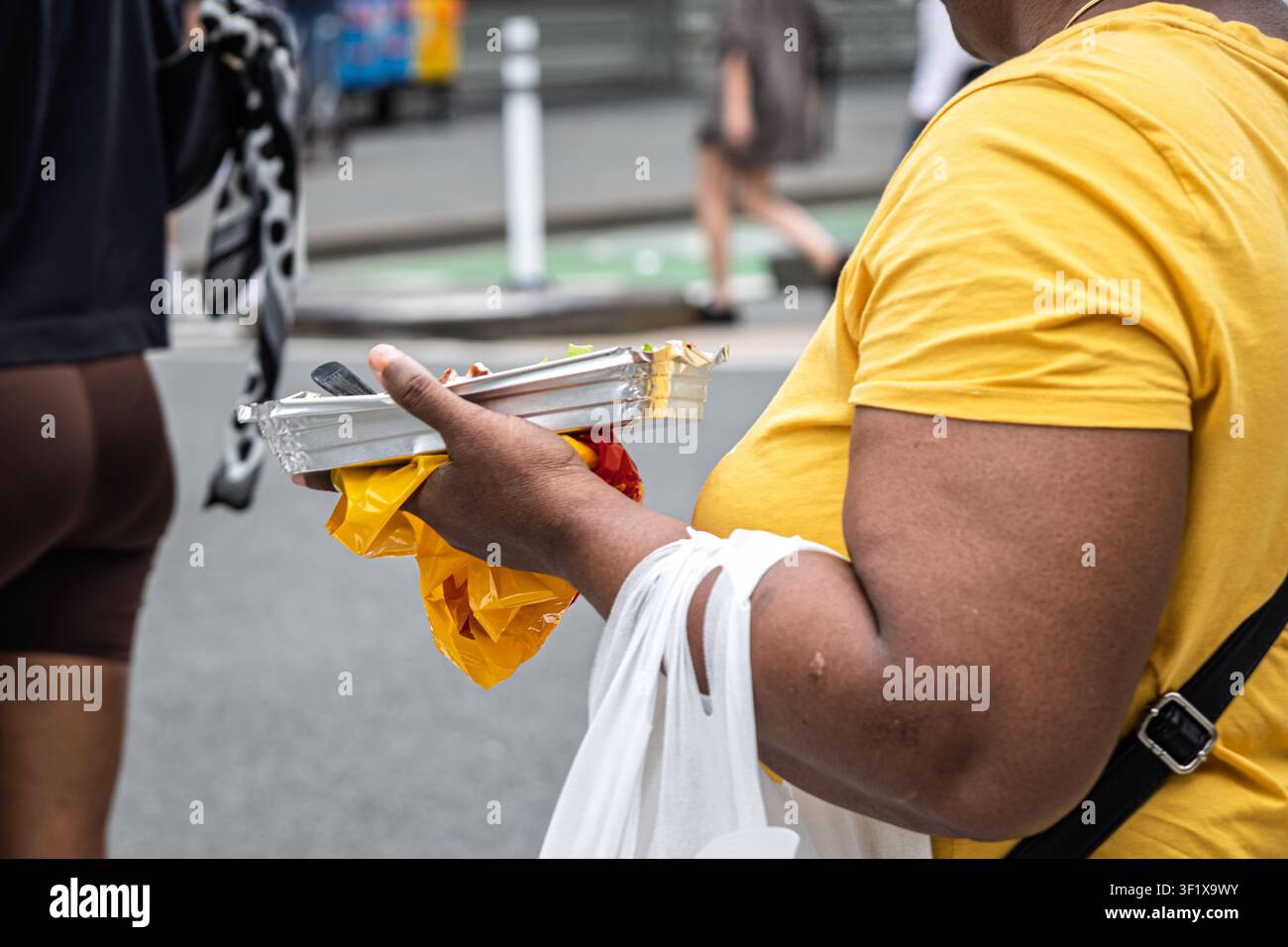 Eine Frau trägt Essen zum Mitnehmen und Plastiktüten über eine Straße in New York City. Stockfoto