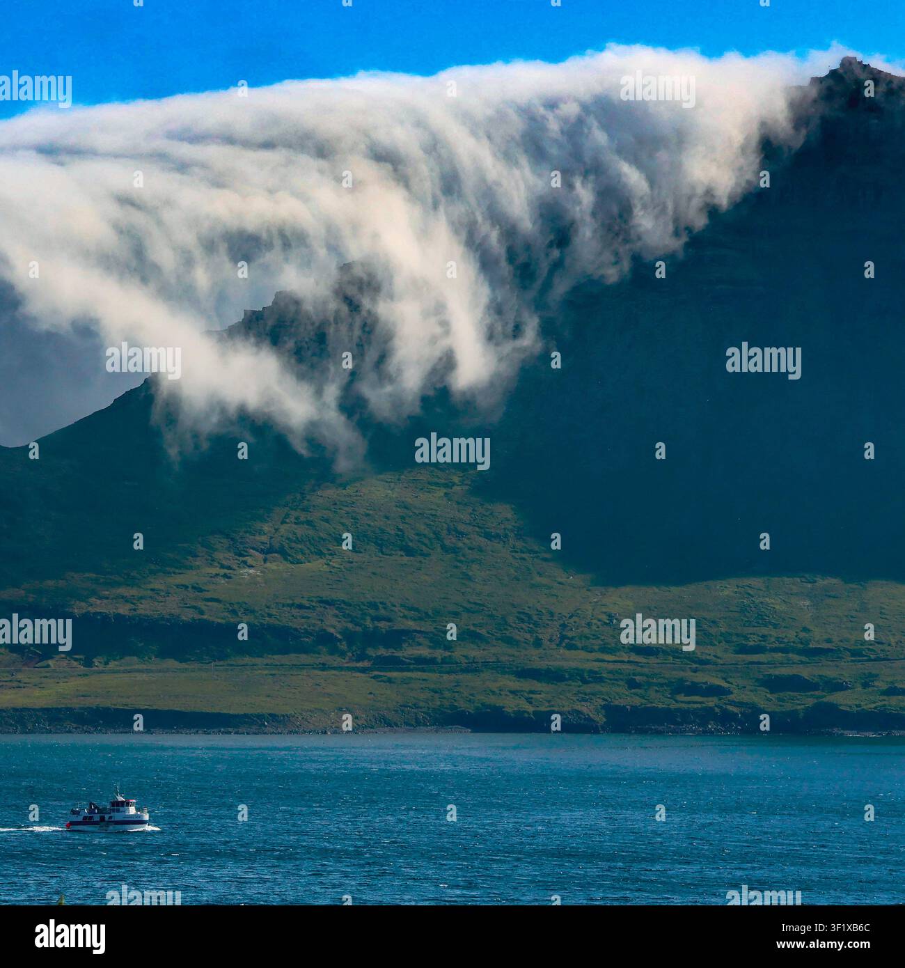 Dramatische tiefe Wolke, die über einen Bergrücken neben einem isländischen Fjord fließt Stockfoto
