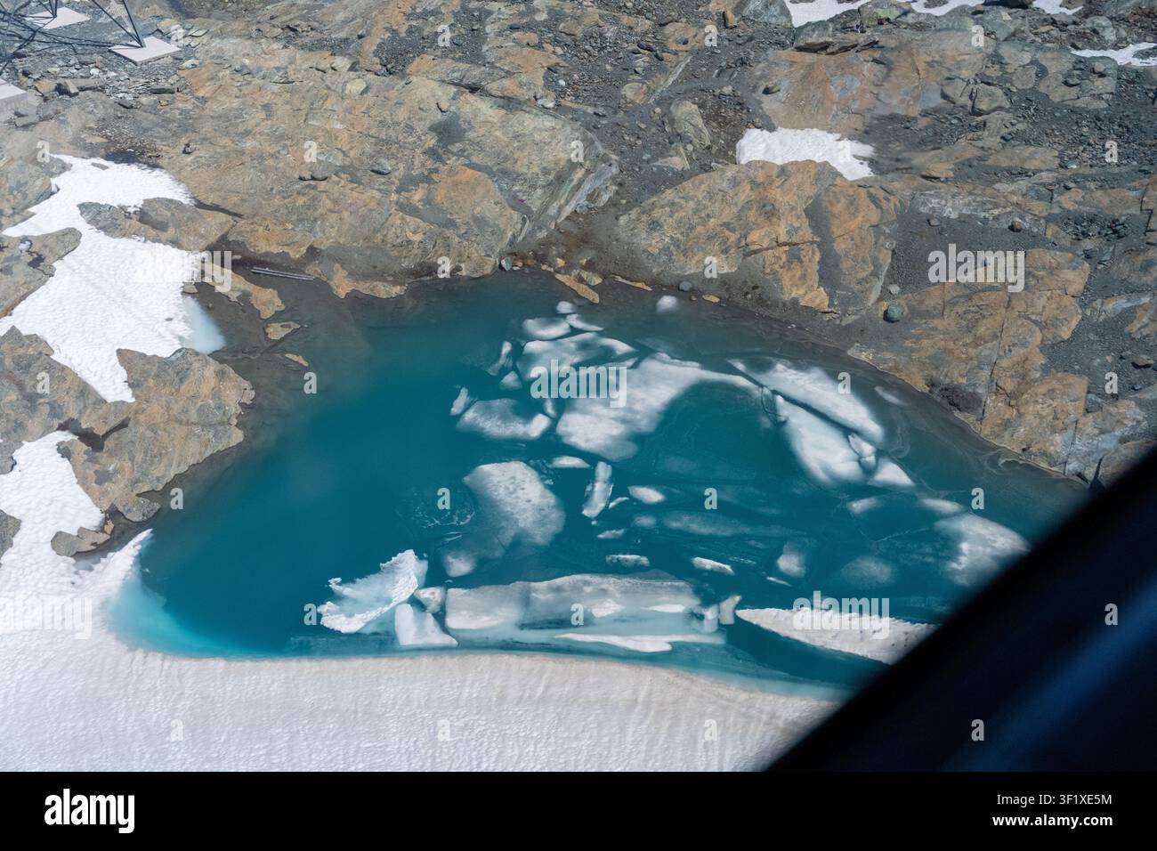 Alpensee mit Eisschollen und türkisblauem Wasser mit felsiger Uferzone und Schneeflecken Stockfoto