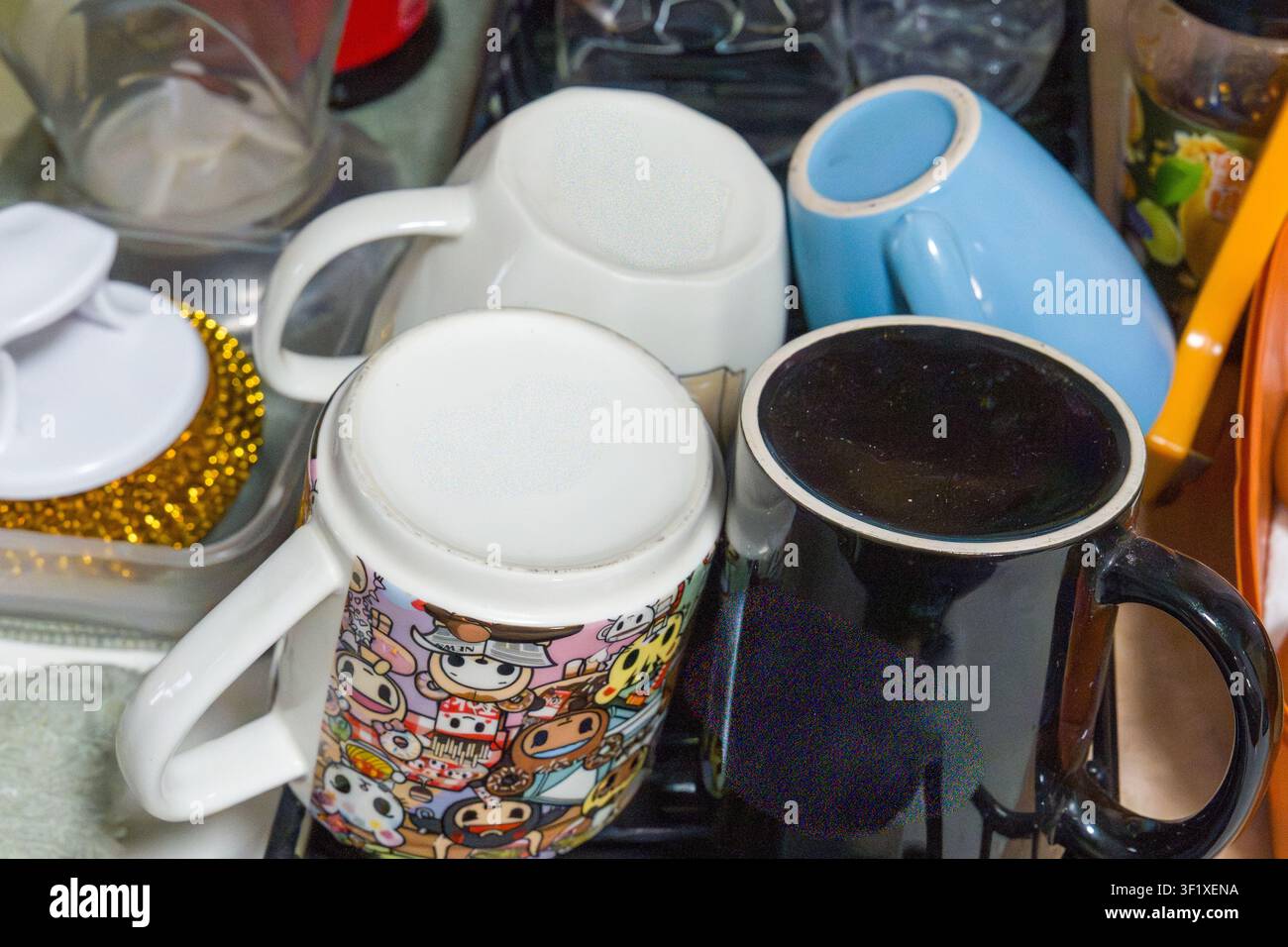 Vier Tassen stehen eng beieinander auf einer Oberfläche. Eine enthält eine dunkle Flüssigkeit, wahrscheinlich Kaffee oder Tee. Eine andere hat bunte Cartoonfiguren darauf gedruckt. Die dritte m Stockfoto