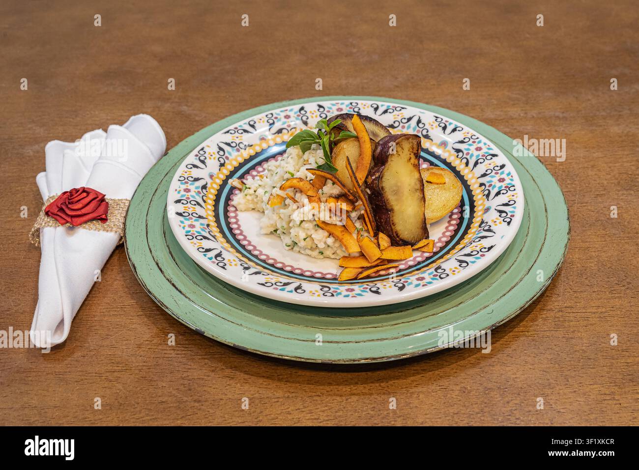 Stillleben mit gebratenen Süßkartoffelscheiben und Reis. Weiches, diffuses Licht betont die Texturen. Holztisch. Teller mit farbenfrohem Muster. Ideal f Stockfoto
