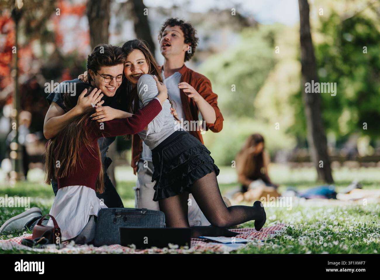 Gruppe junger Freunde, die sich während eines Picknicks in einem sonnigen Park umarmen und lachen Stockfoto