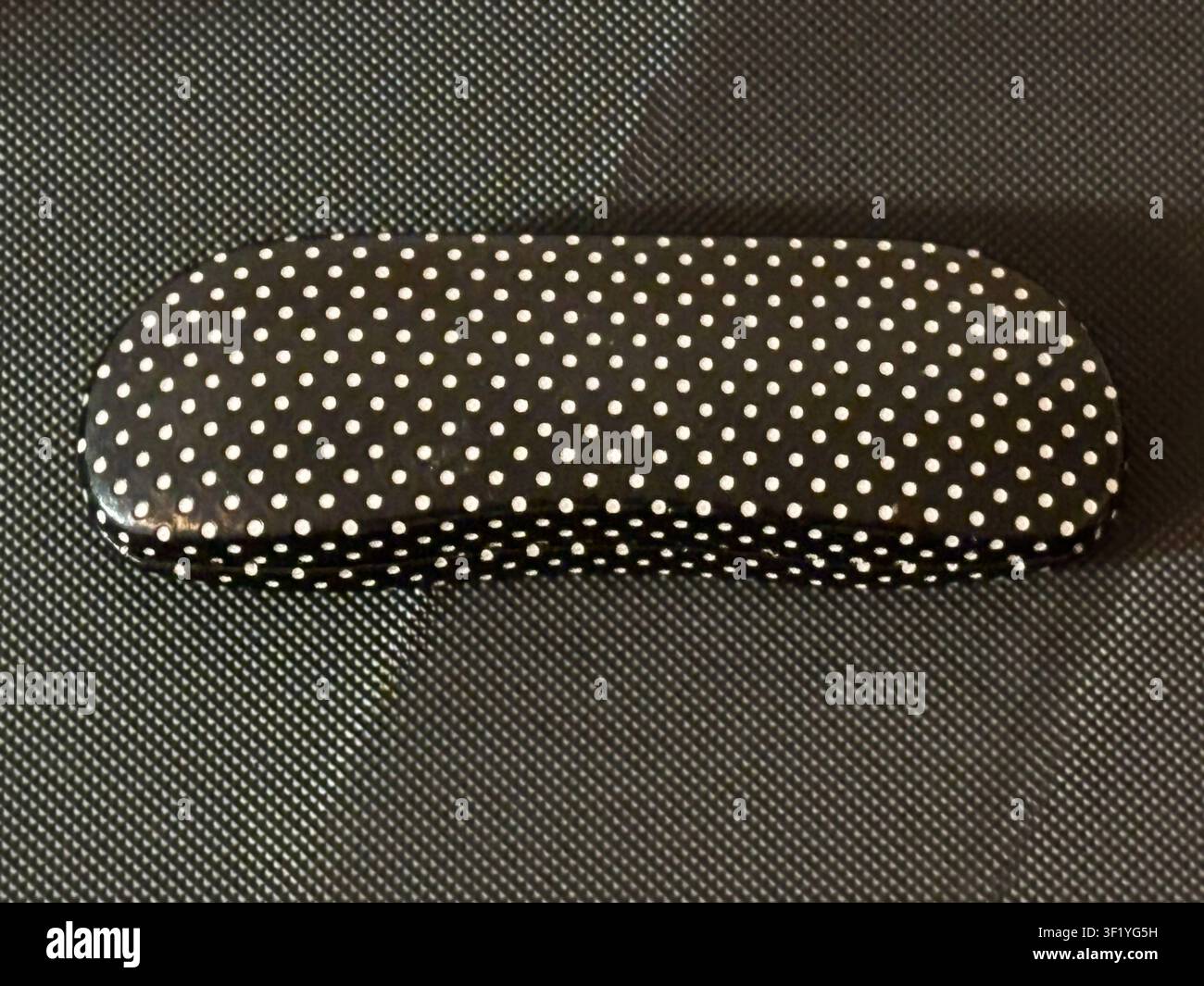 Ein Eyebobs-Gläseretui mit einem schwarz-weißen Tupfenmuster, das auf einem ähnlichen Hintergrund fotografiert wurde. Stockfoto