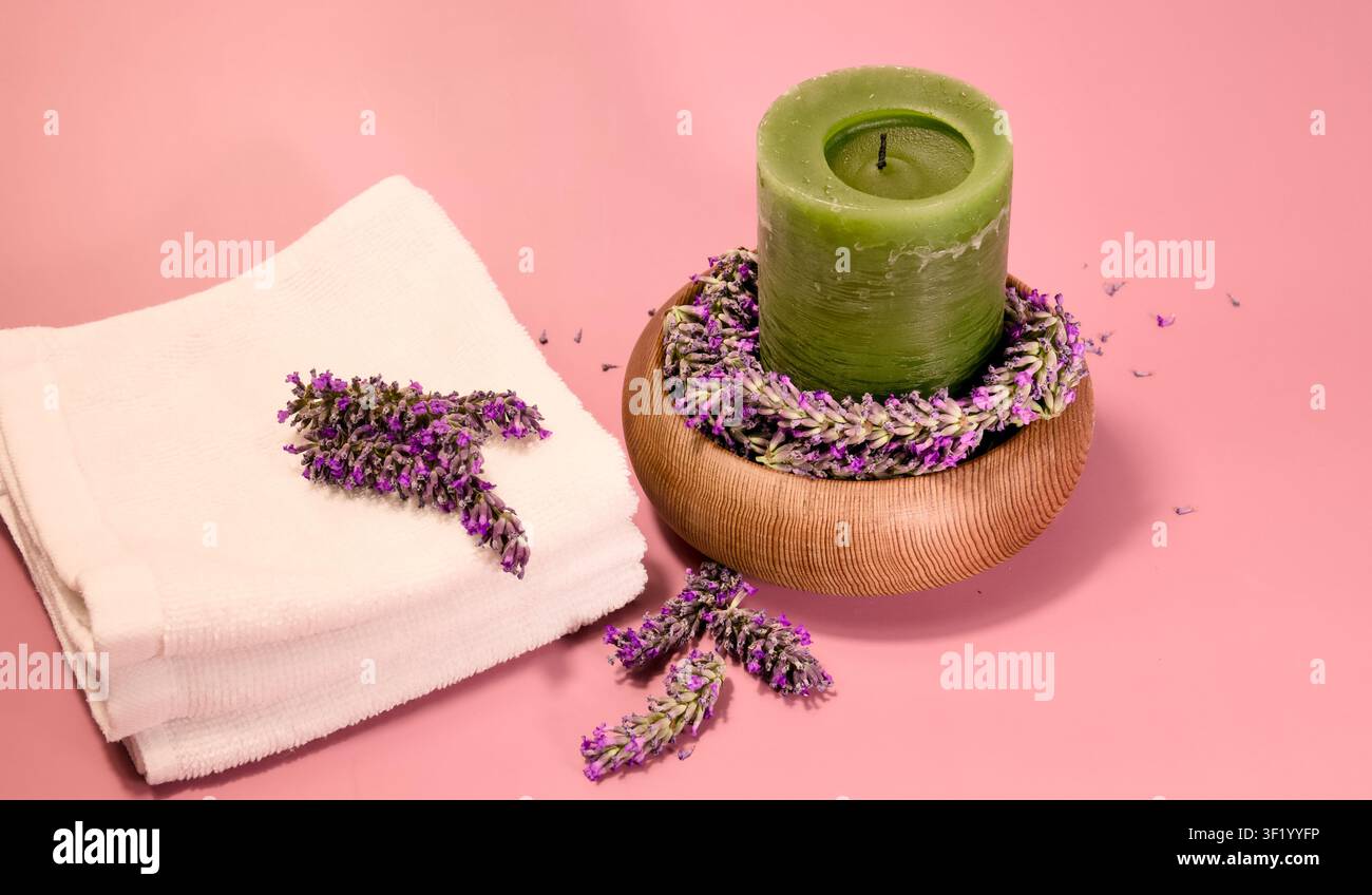 Eine spa-ähnliche Anordnung zeigt einen Stapel weißer Handtücher, eine grüne Stumpenkerze, die auf einer hölzernen Schale mit Lavendel ruht Stockfoto