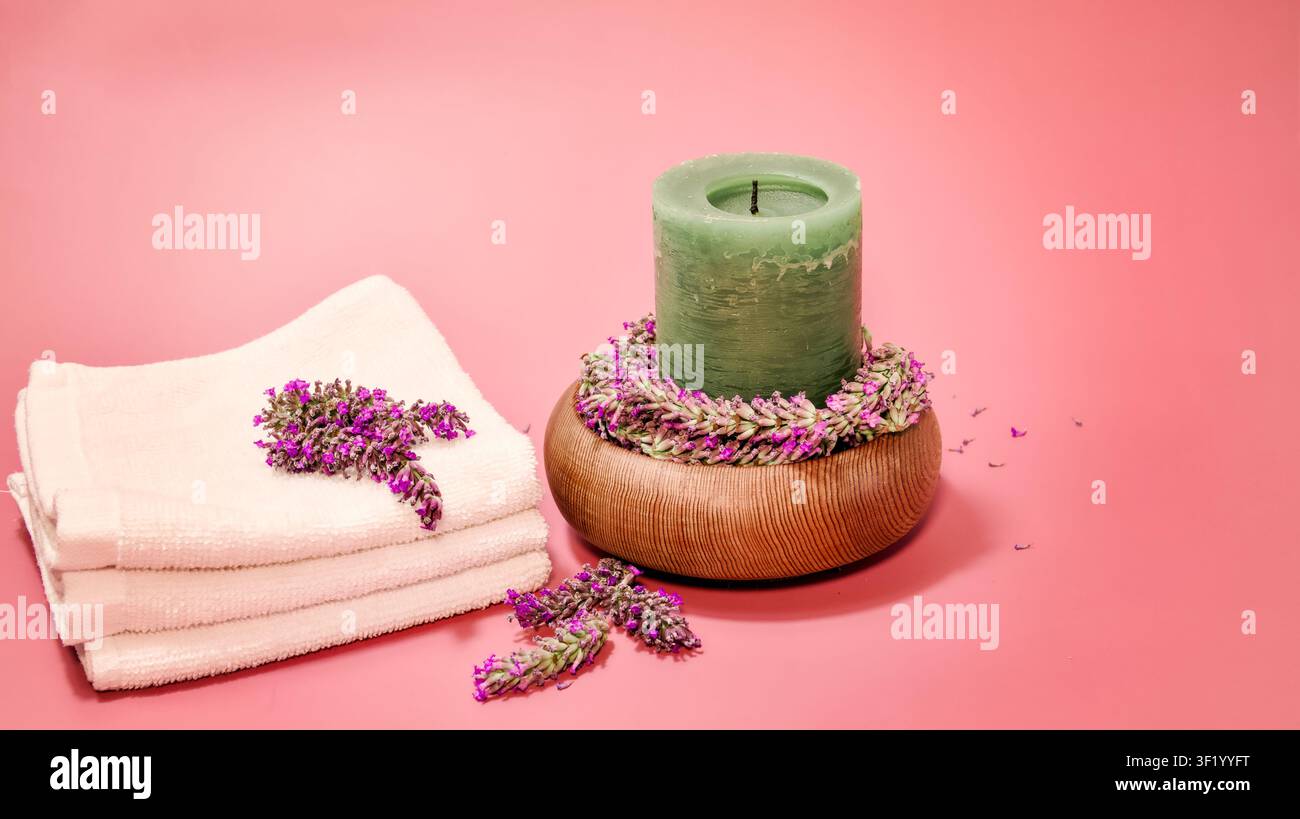 Eine ruhige Spa-Einrichtung umfasst ordentlich gefaltete weiße Handtücher und eine grüne Stumpenkerze, die auf einer Holzschale platziert ist Stockfoto