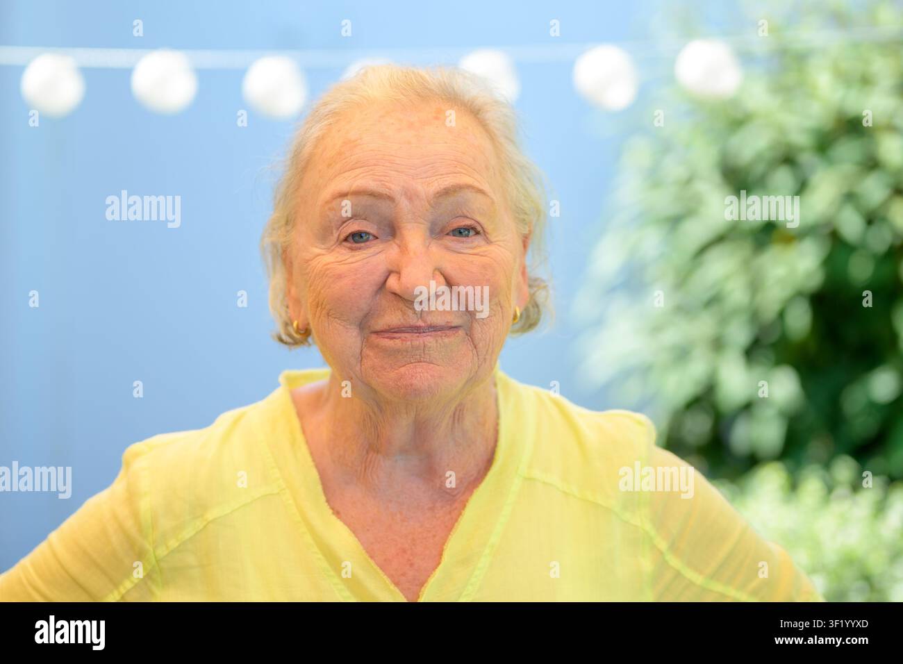 Eine ältere Frau mit einem warmen Ausdruck schaut selbstbewusst in die Kamera in einer entspannten häuslichen Umgebung. Stockfoto