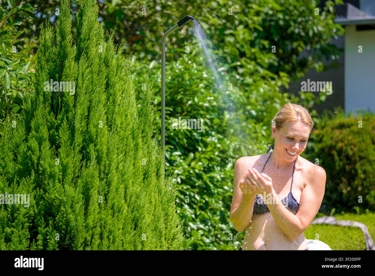 Lächelnde Frau genießt eine erfrischende Außendusche im Garten an einem heißen Sommertag. Stockfoto