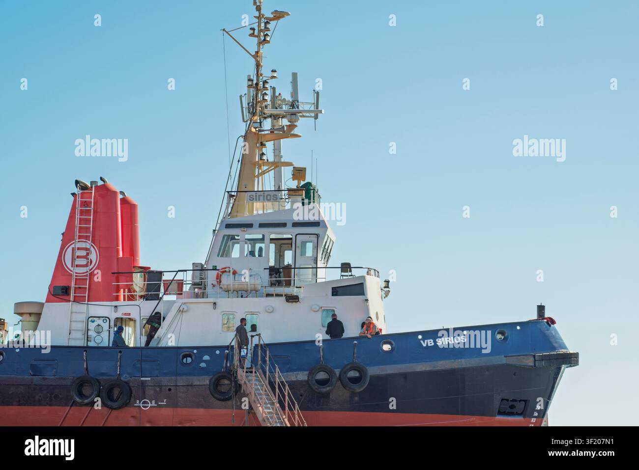 Das Schleppboot VB SIRIOS liegt im Hafen von Burriana, Castello, Spanien, und präsentiert seine Industrieausrüstung und den roten Schornstein unter einem klaren Himmel. Stockfoto