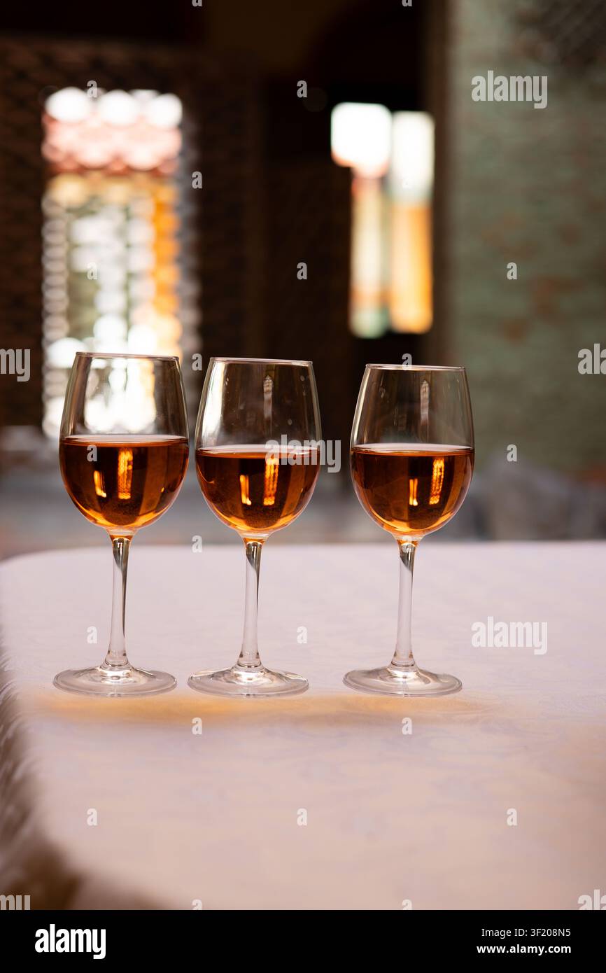 Drei Stielgläser gefüllt mit einem bernsteinfarbenen alkoholischen Getränk, arrangiert auf einem Restauranttisch. Elegante Gastgewerbe-Stillleben mit warmem Am Stockfoto
