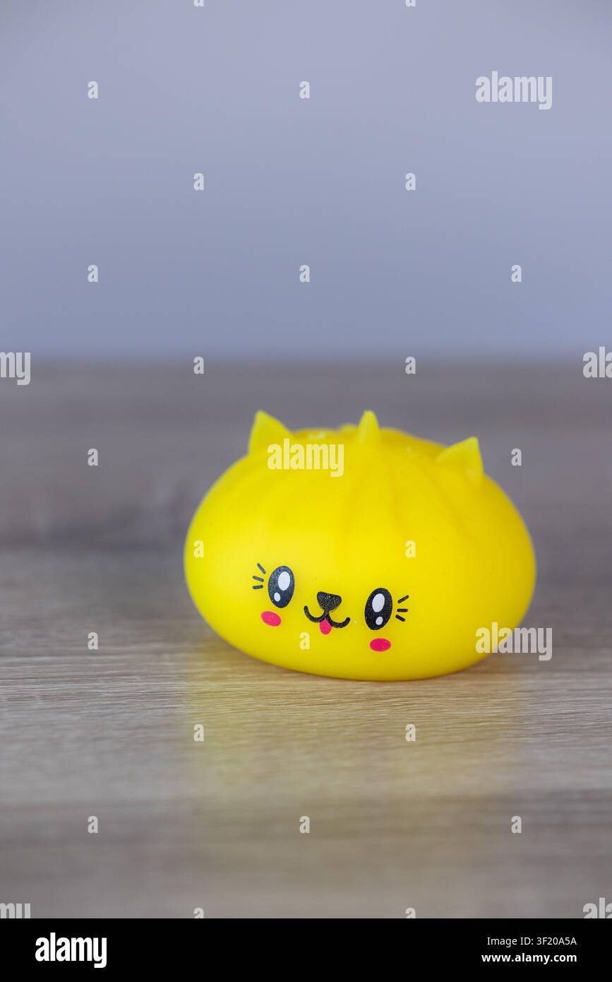 Niedliches gelbes Kawaii-Slime-Spielzeug mit lächelndem Katzen-Gesicht auf Holztablett Stockfoto